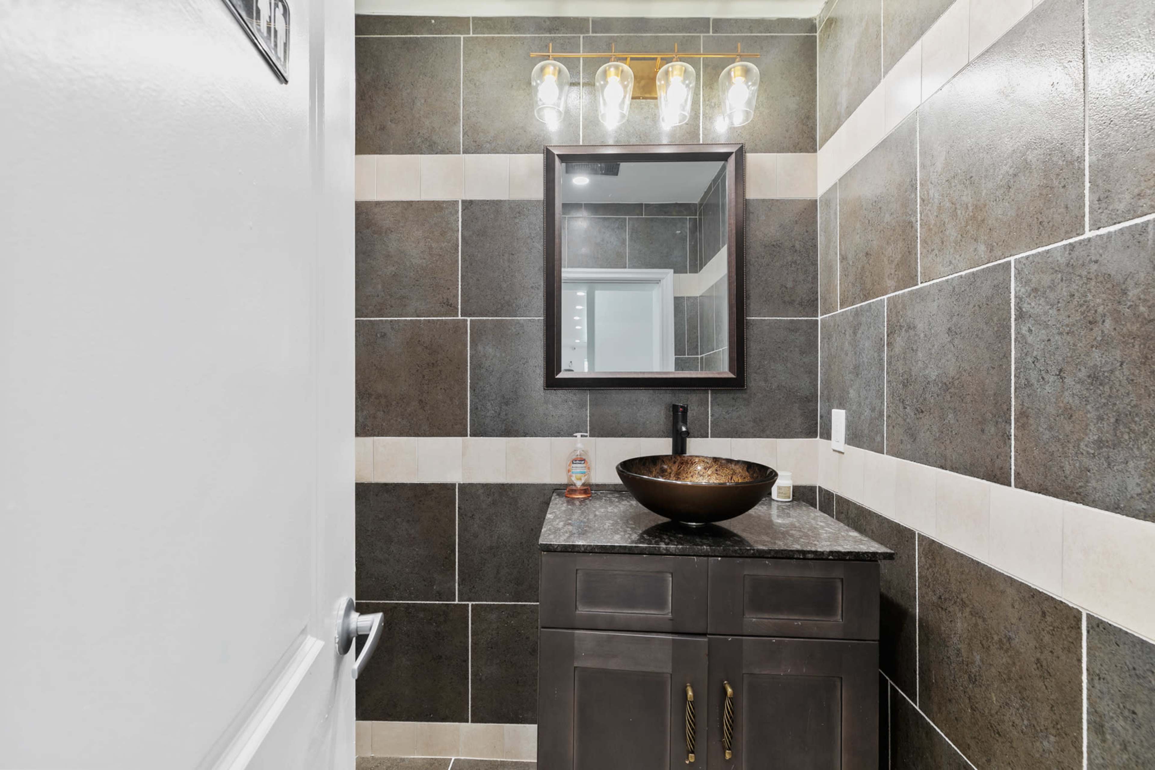 A modern bathroom features a dark cabinetry with a circular sink, a wall-mounted mirror, and stylish light fixtures above the sink area.