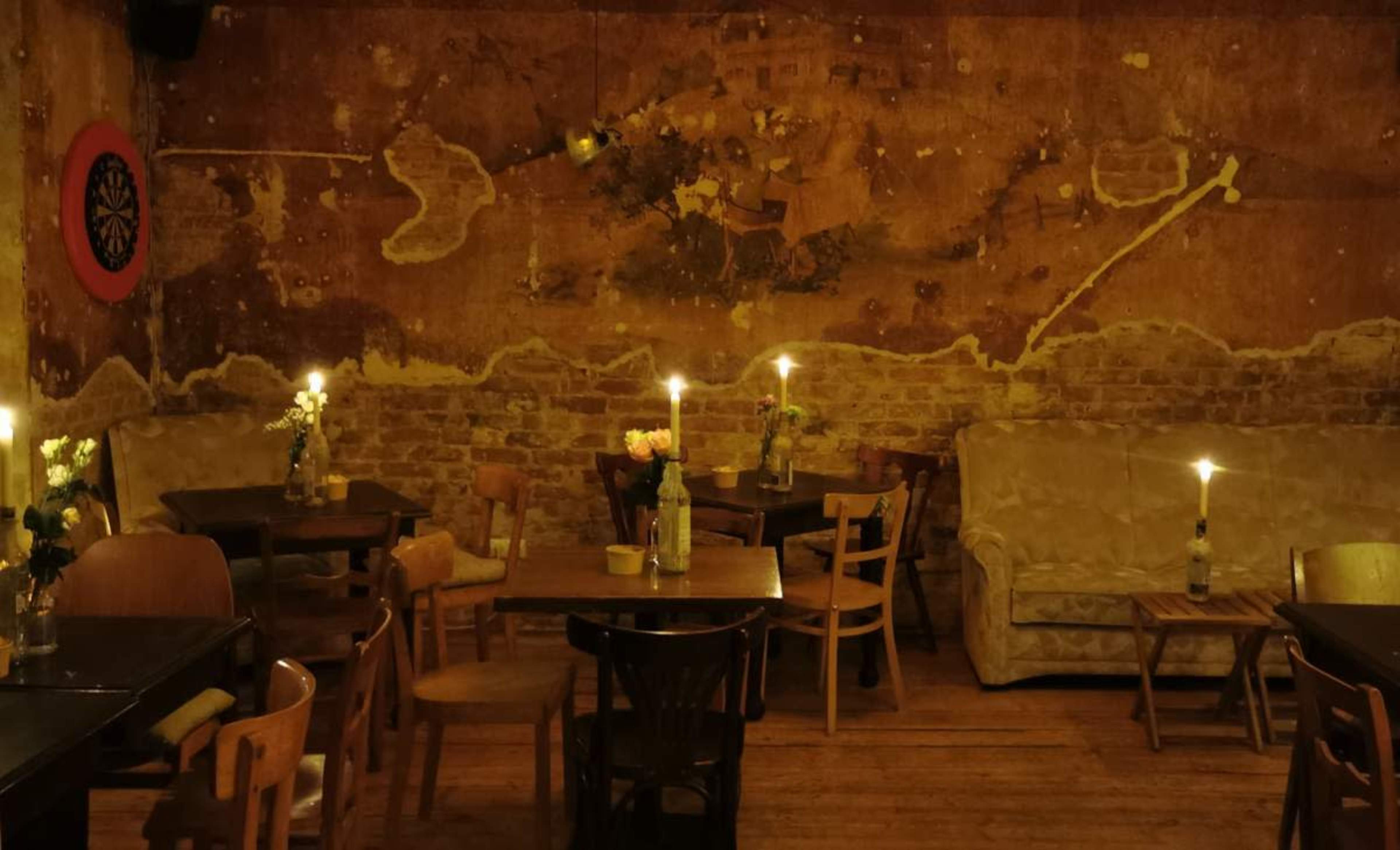 The image shows a dimly lit, vintage-style café with wooden tables, chairs, and a decorative mural on the wall.