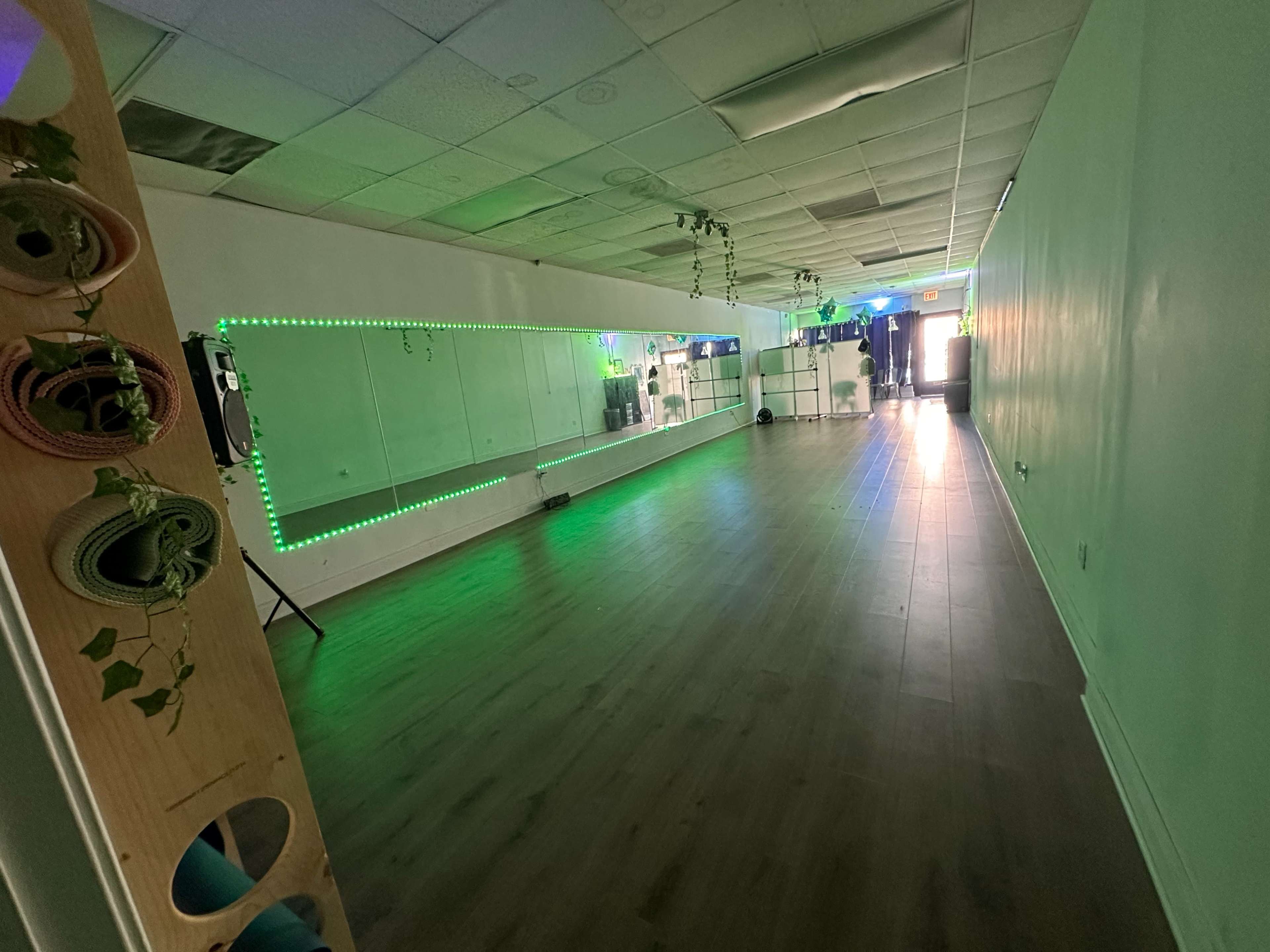 The image shows an empty yoga or dance studio with green LED lighting and mirrors along one wall.