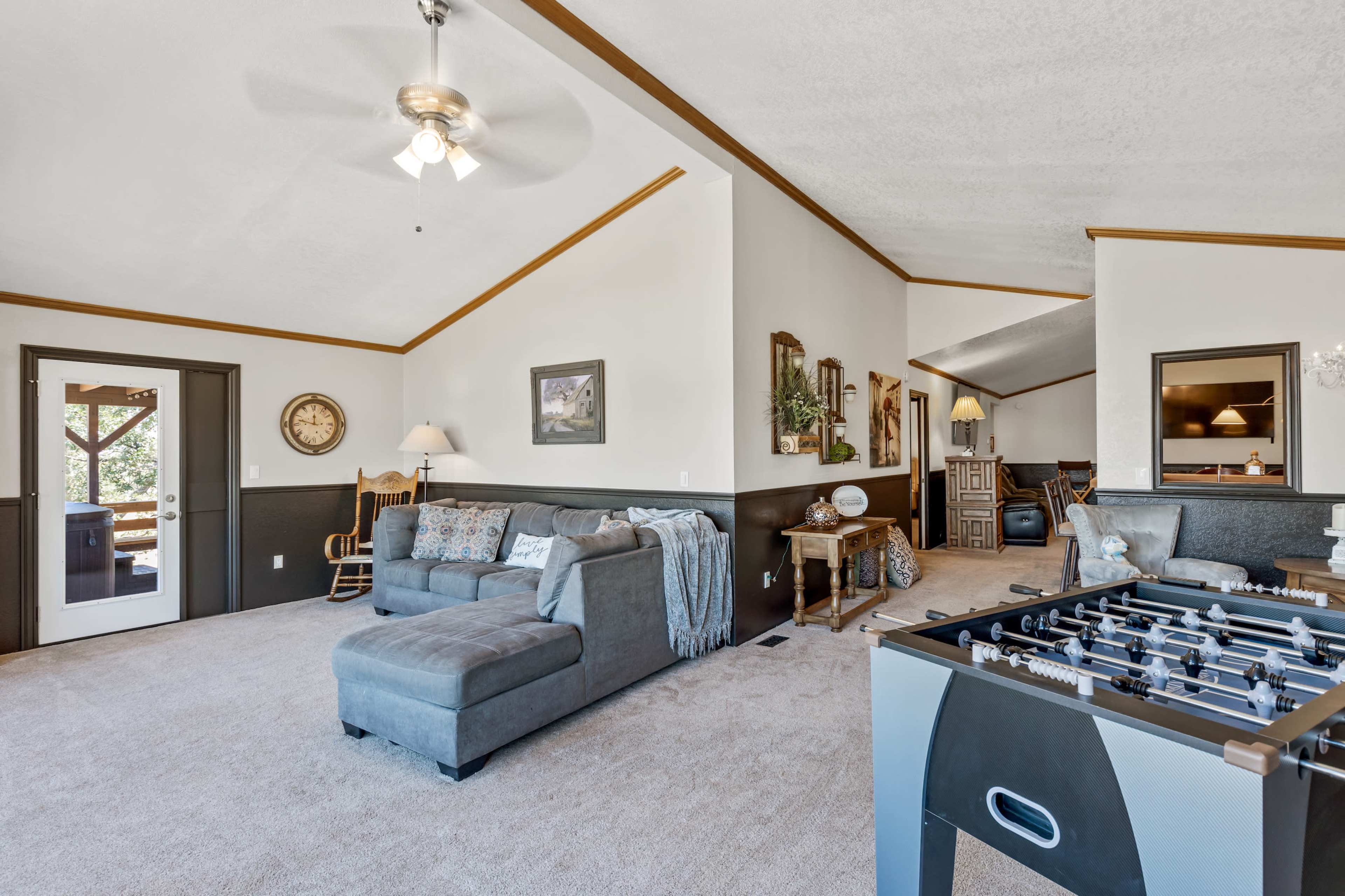 A spacious living room with a sectional sofa, a foosball table, and large windows letting in natural light.