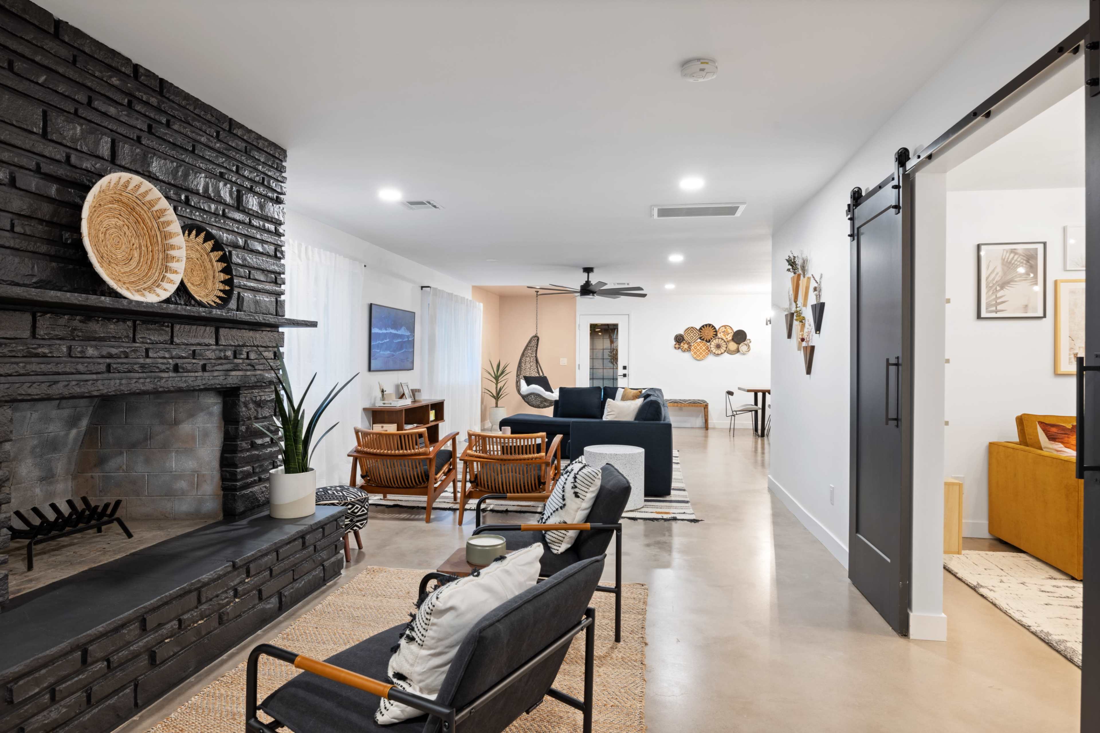 A modern living space featuring a stone fireplace, seating area with wooden chairs, and a partially visible adjacent room with decorative wall art.