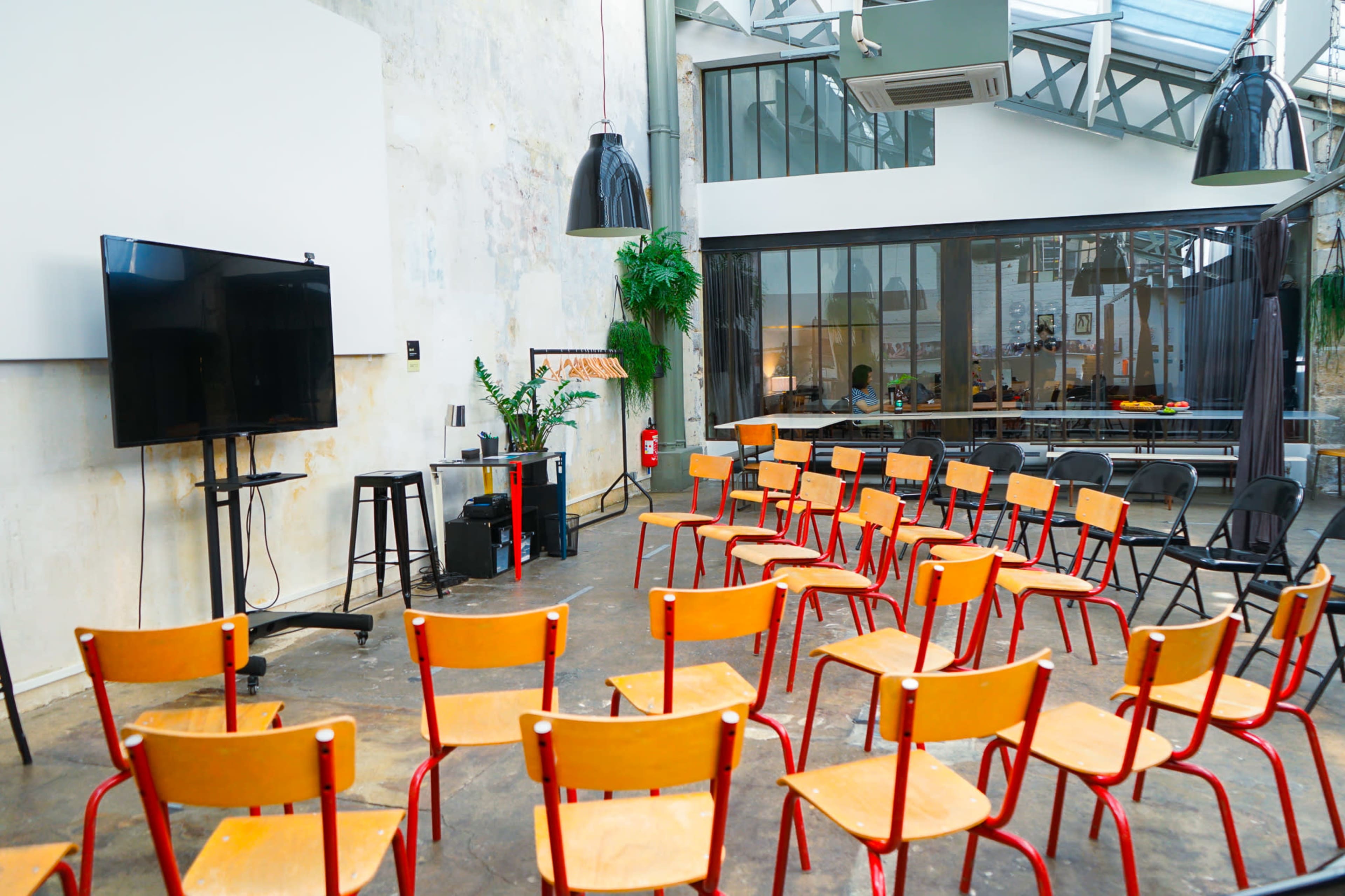 A spacious room features rows of wooden chairs arranged for a presentation, with a television and sound equipment set up at one end.