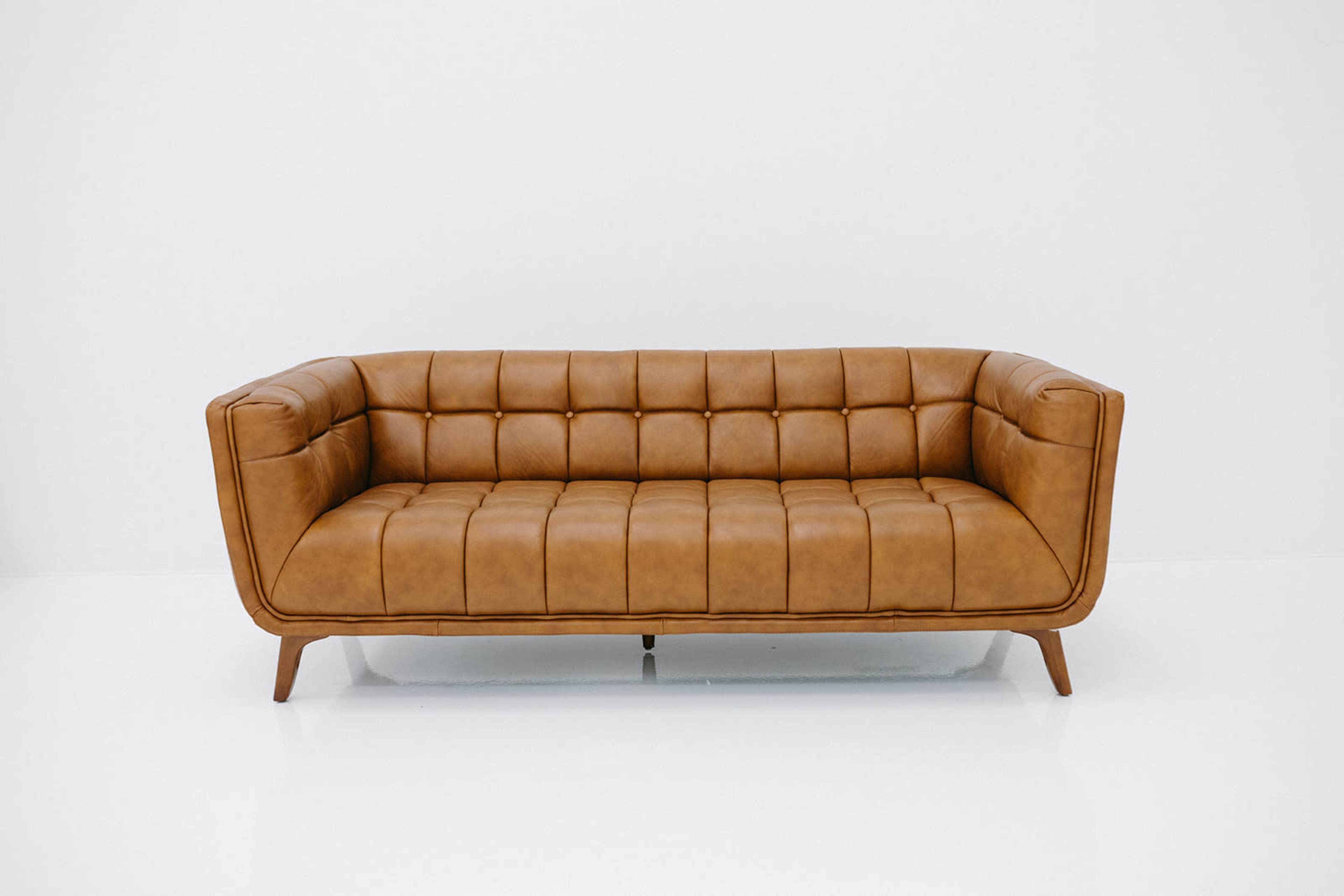 A brown leather sofa with tufted upholstery and wooden legs against a white background.