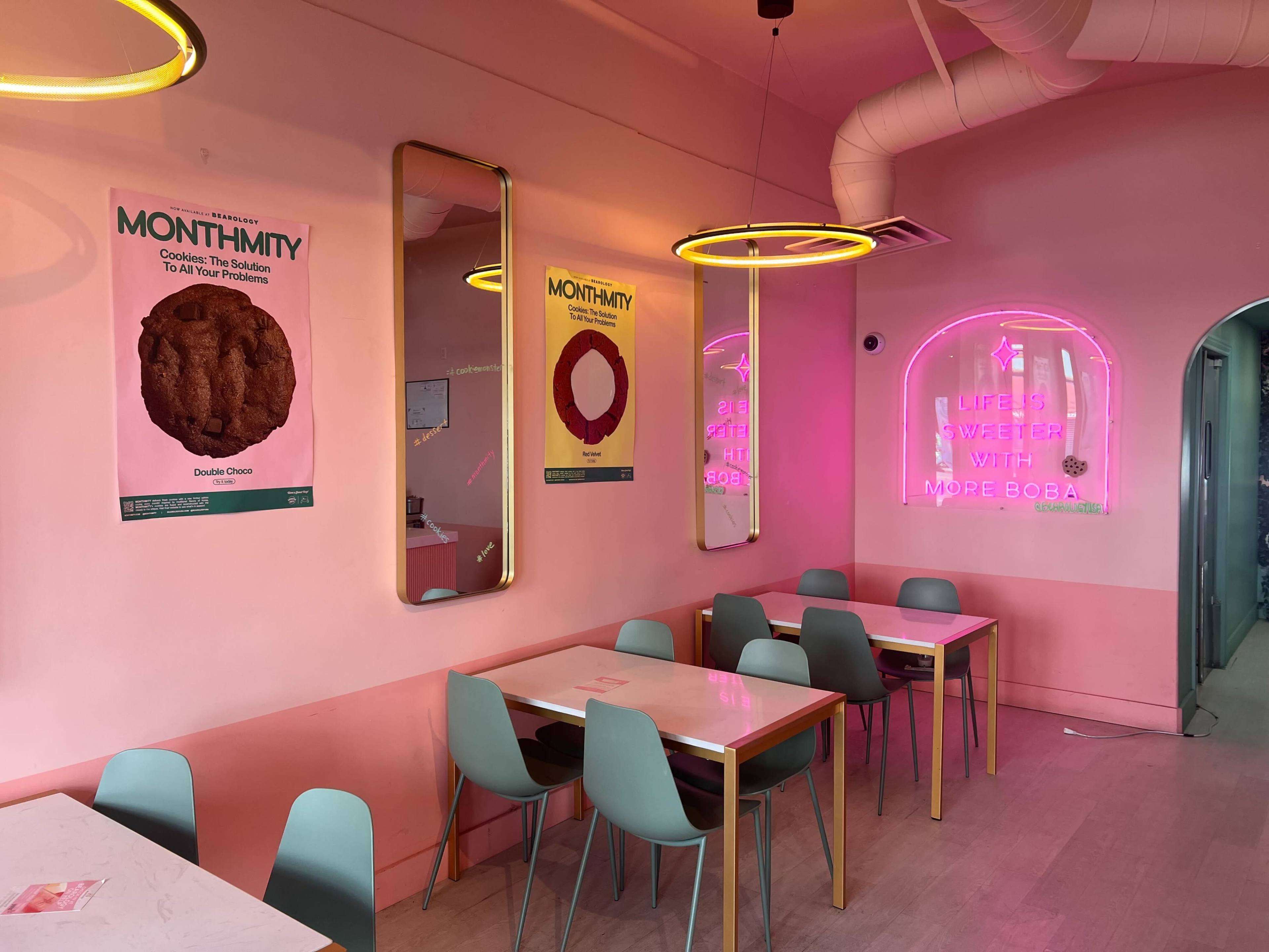 A brightly lit café with pink walls, modern seating, and decorative mirrors featuring colorful posters.