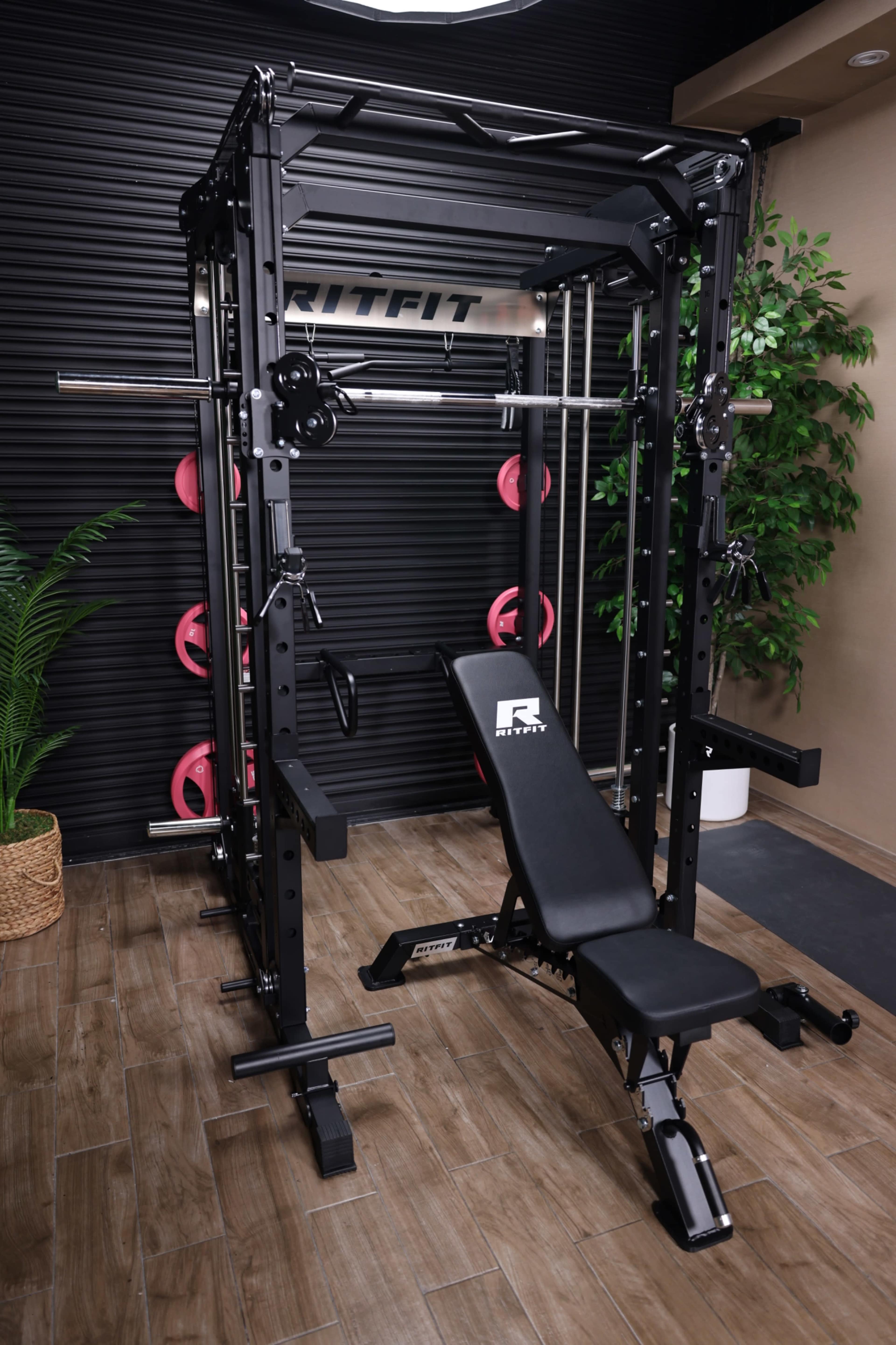 The image shows a multi-functional weightlifting machine with a bench, weights, and a sleek black design, positioned in a well-lit room with indoor plants.