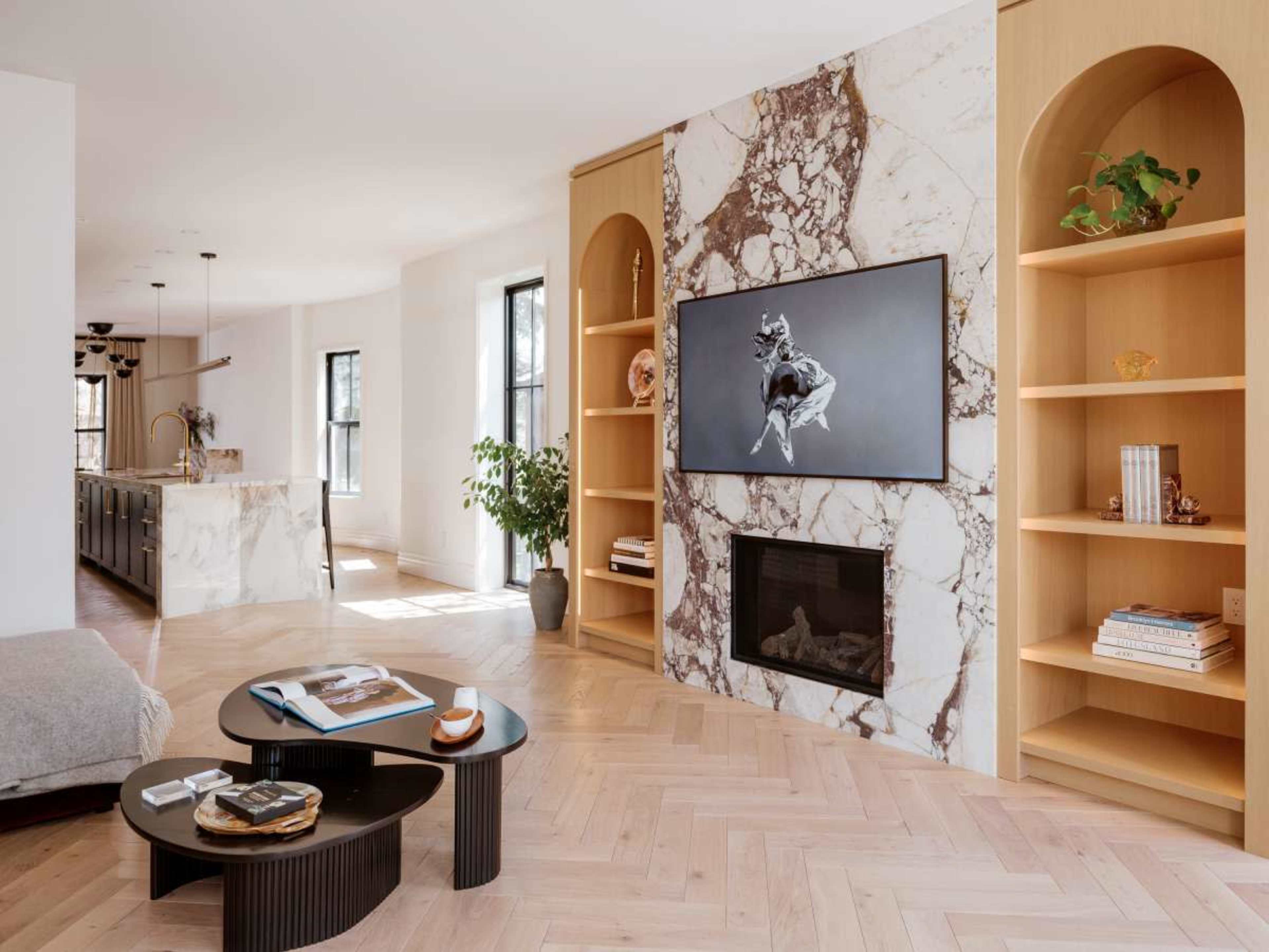 The living room features a marble wall with a large flat-screen TV, flanked by built-in shelves, and a modern coffee table in front of a sofa.