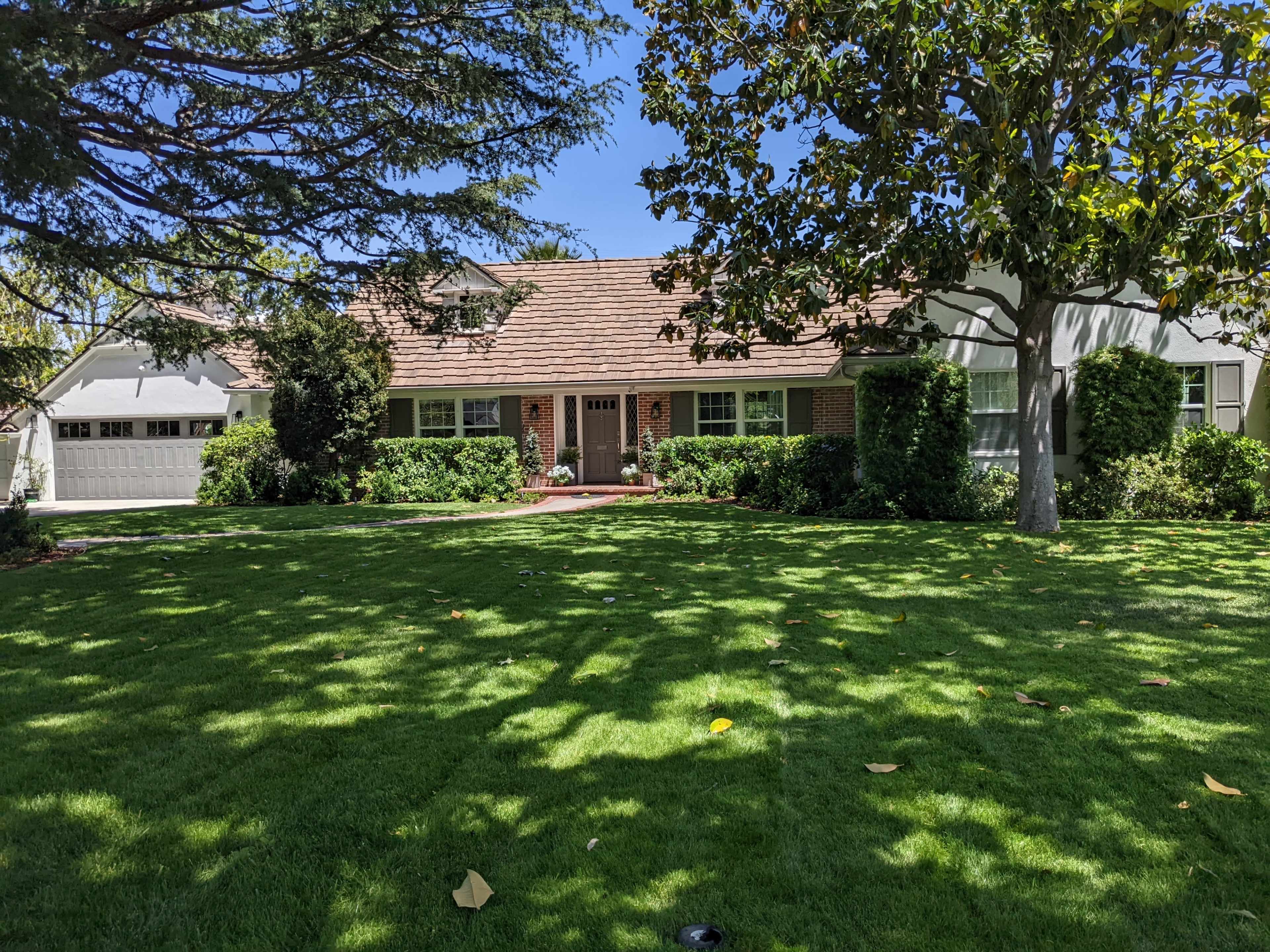 A front view of a house with a manicured lawn and trees surrounding it.