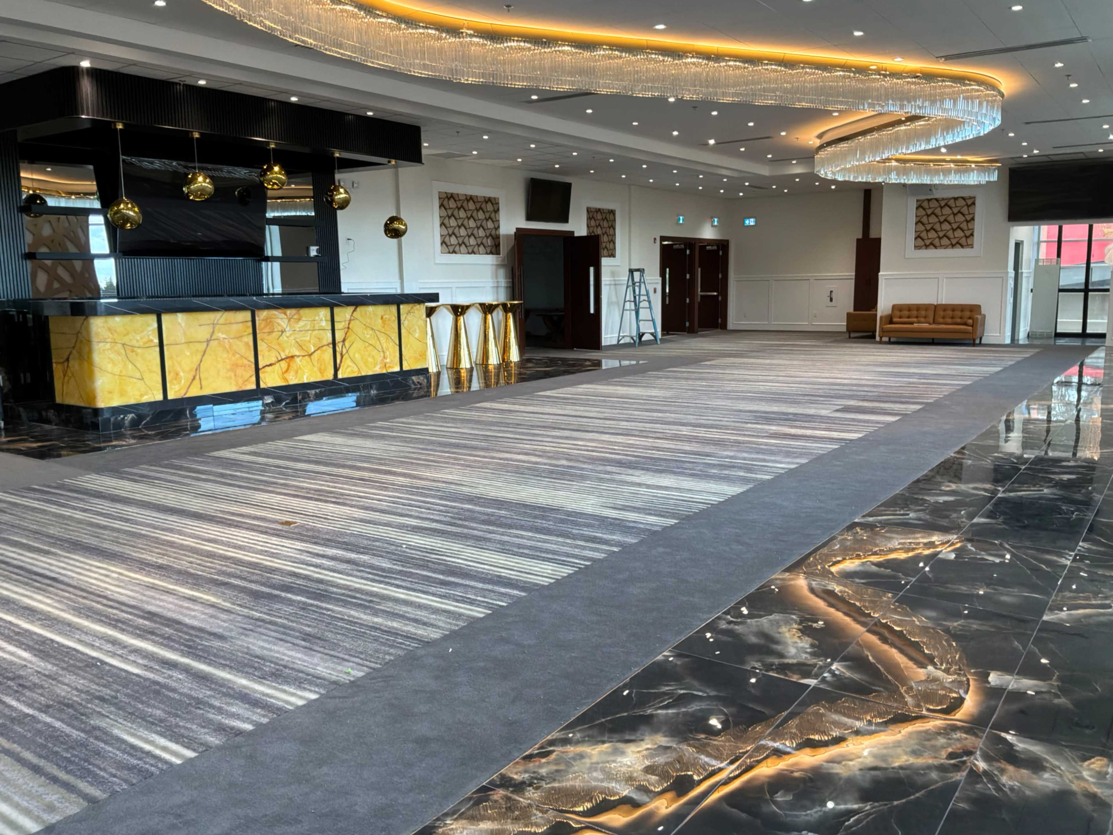 The image shows an empty, modern event space featuring a bar area with round pendant lights, a patterned carpet, and polished marble flooring.