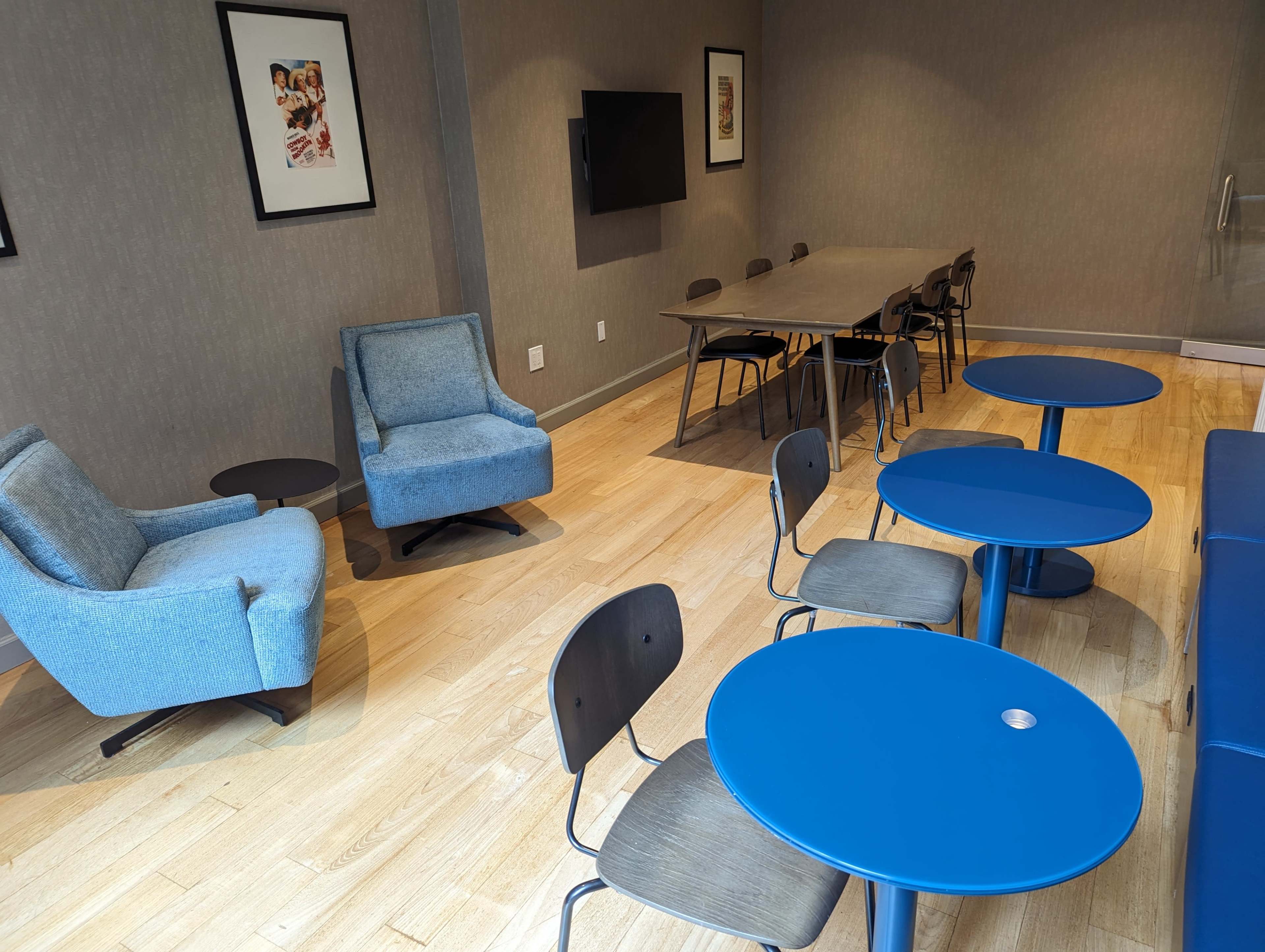 A well-lit room featuring two blue armchairs, several blue tables, black chairs, a large table, and framed artwork on the walls.