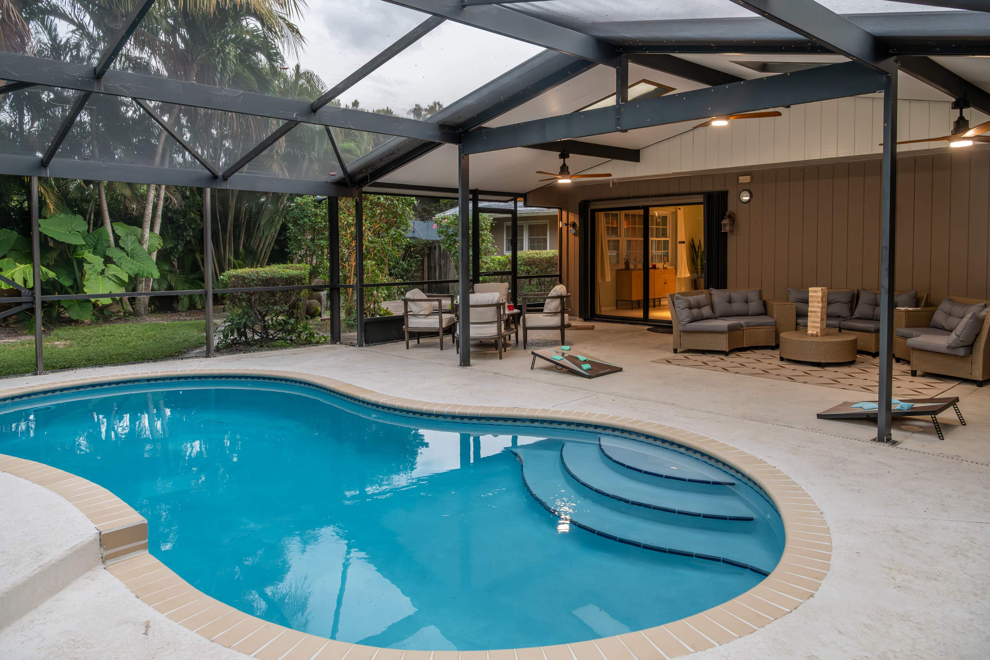 The image shows a screened-in backyard with a swimming pool, adjacent seating area, and lush greenery.