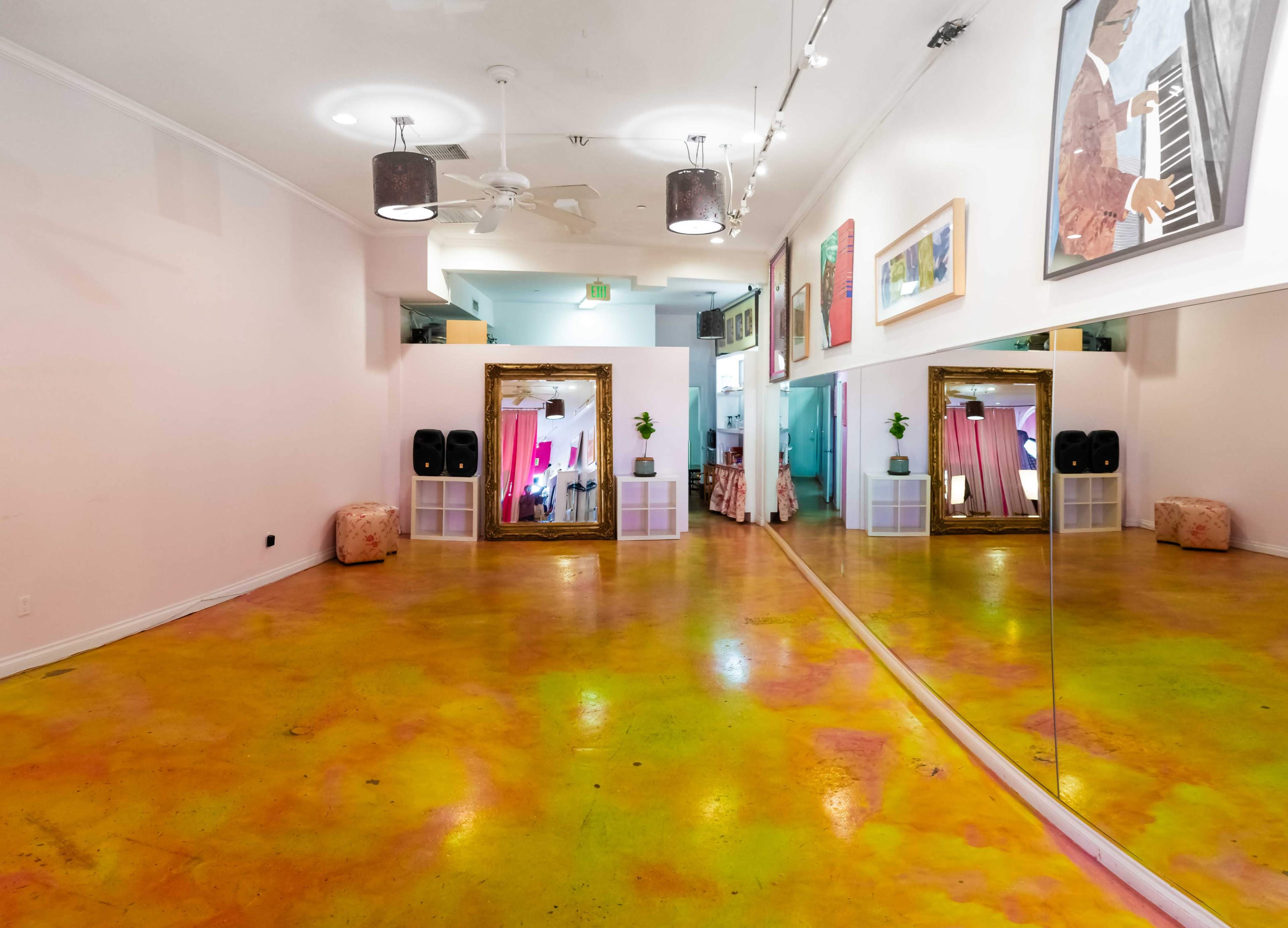 The image shows an empty room with colorful polished concrete flooring, a large decorative mirror, and various pieces of art on the walls.