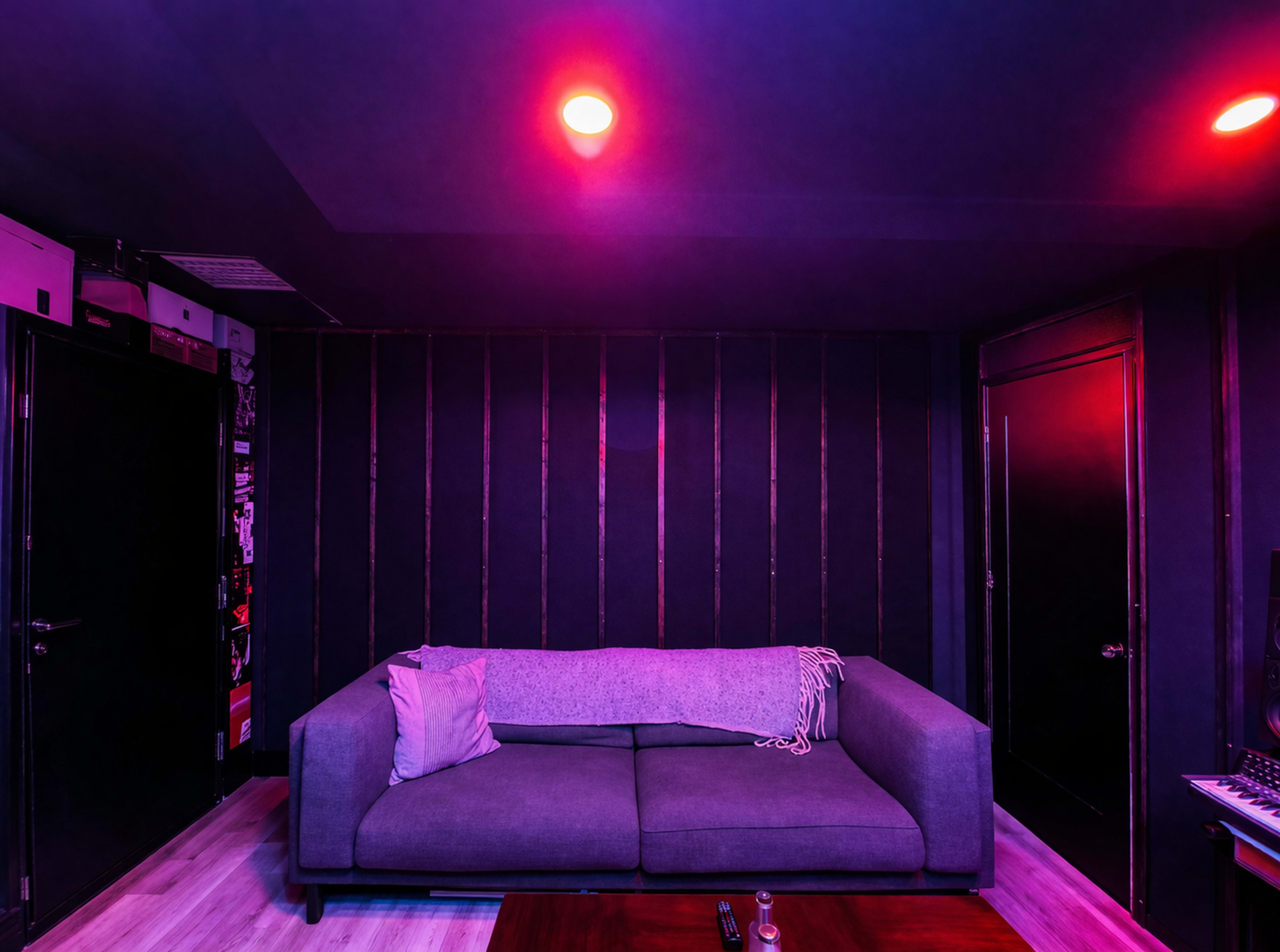 A gray sofa is positioned against a dark wall in a dimly lit room with purple and pink lighting.