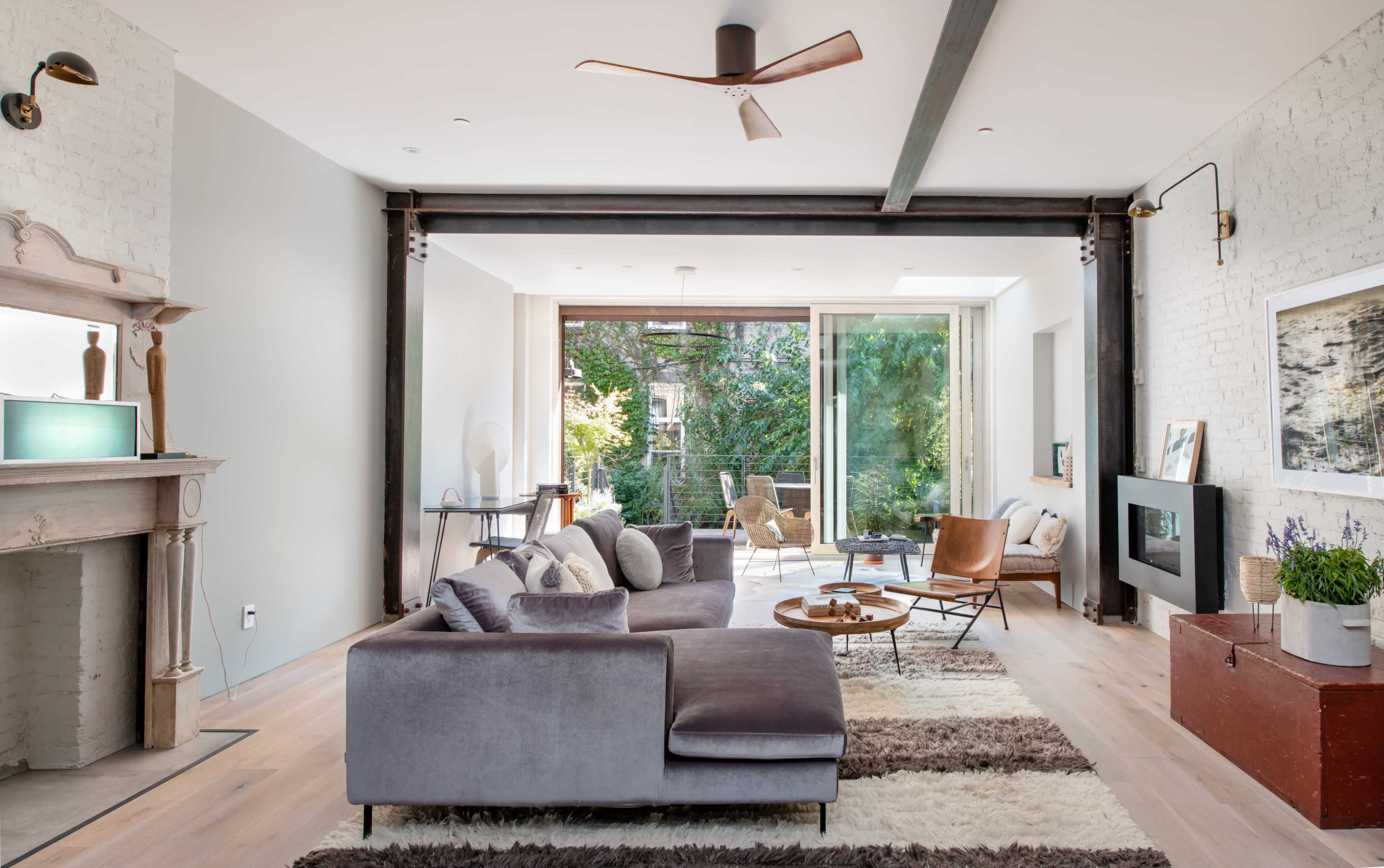 A modern living room features a gray sectional sofa, a wooden coffee table, and large windows that open to a balcony with greenery outside.