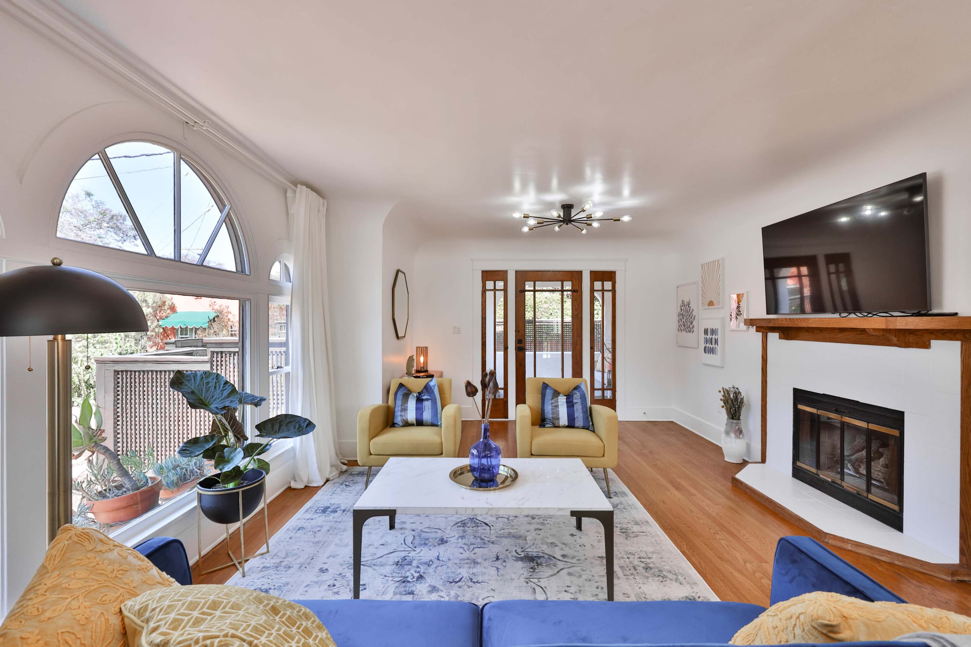 A bright living room featuring a blue sofa, yellow accent chairs, a coffee table, a fireplace, and large windows.