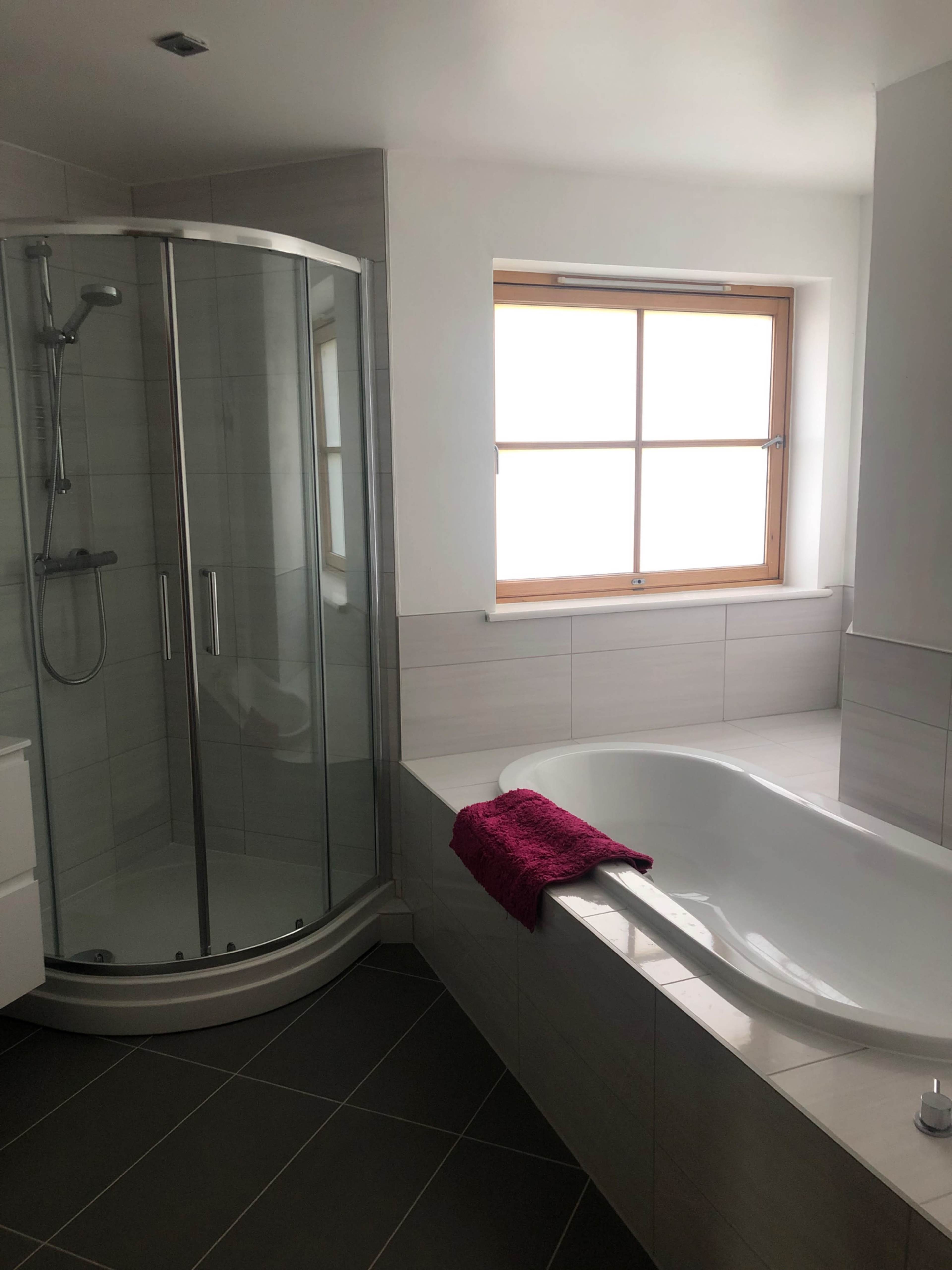 A modern bathroom featuring a glass shower stall and a white bathtub next to a window.