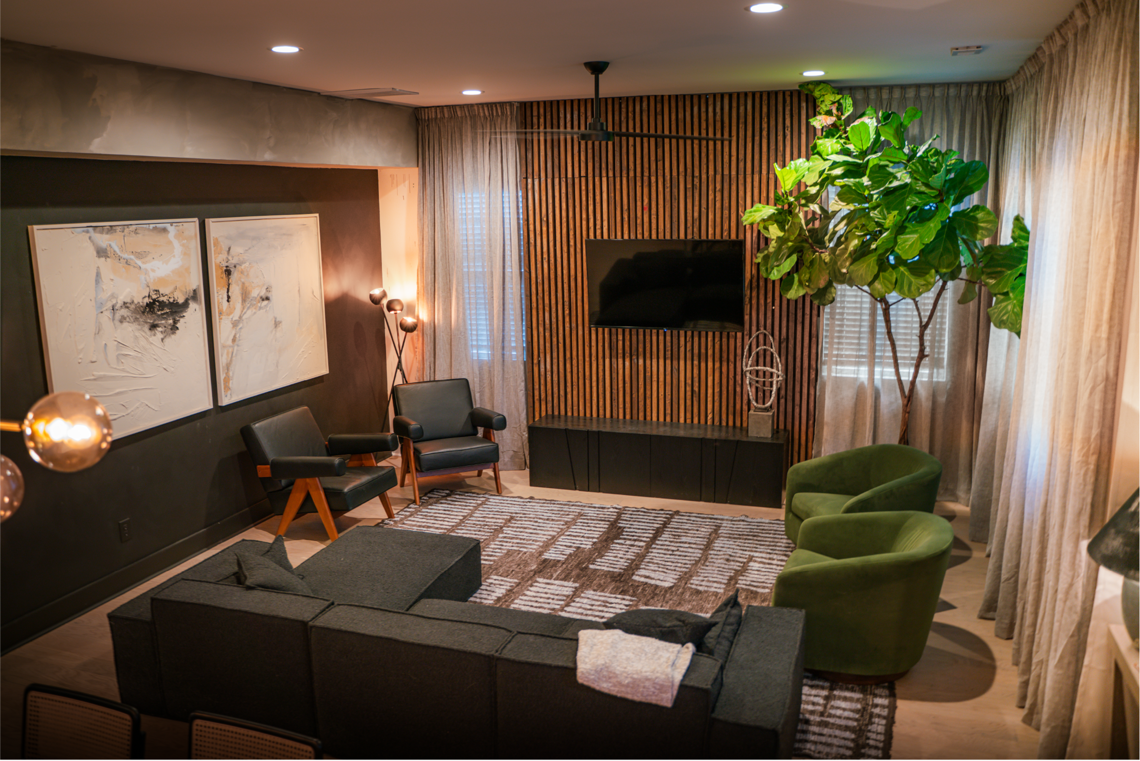 The living room features a sectional couch, two chairs, a large rug, a flat-screen TV mounted on a wooden accent wall, and a potted plant in the corner.