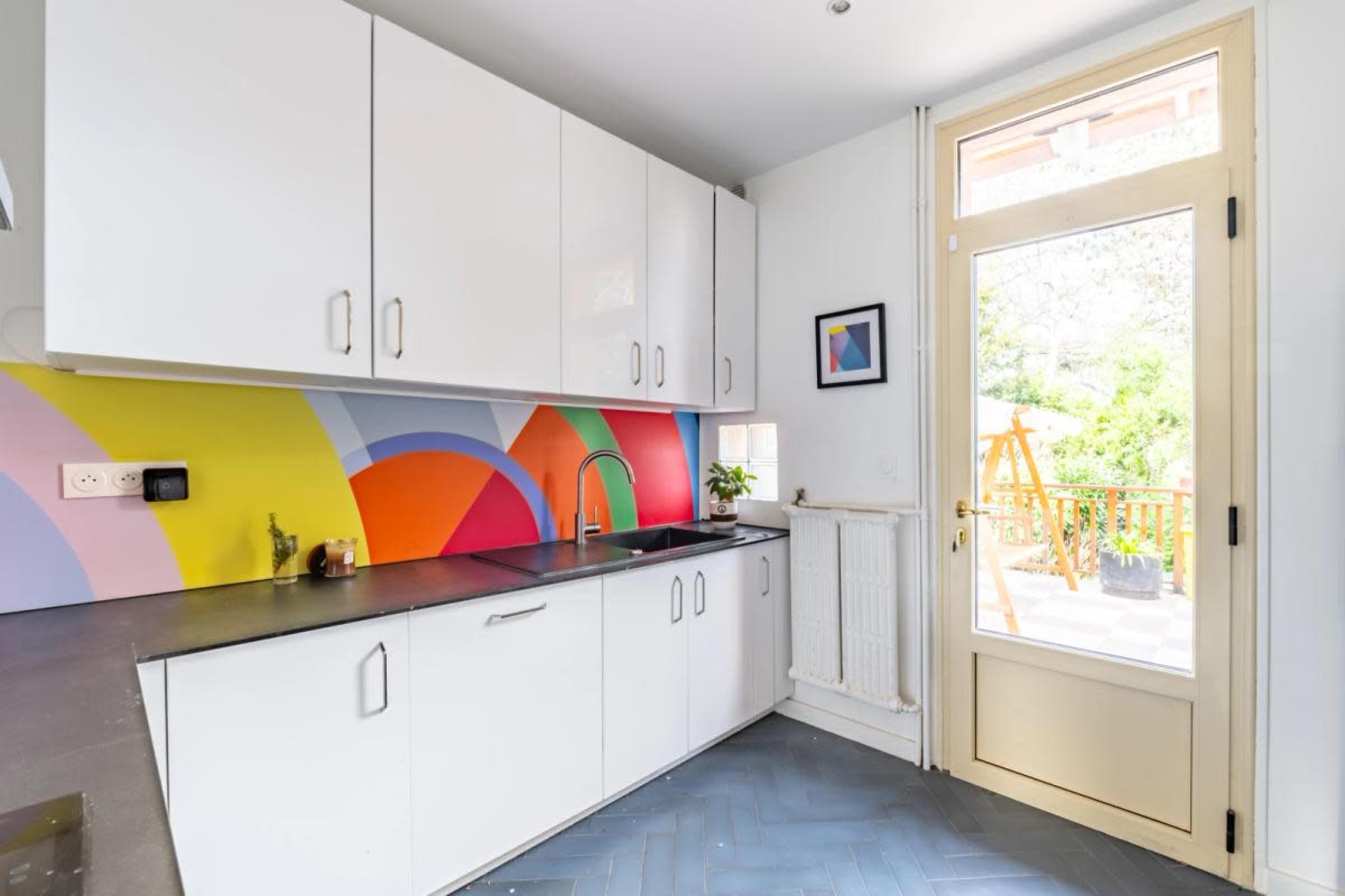 A kitchen features white cabinetry, a colorful backsplash, and a door leading to an outdoor area.