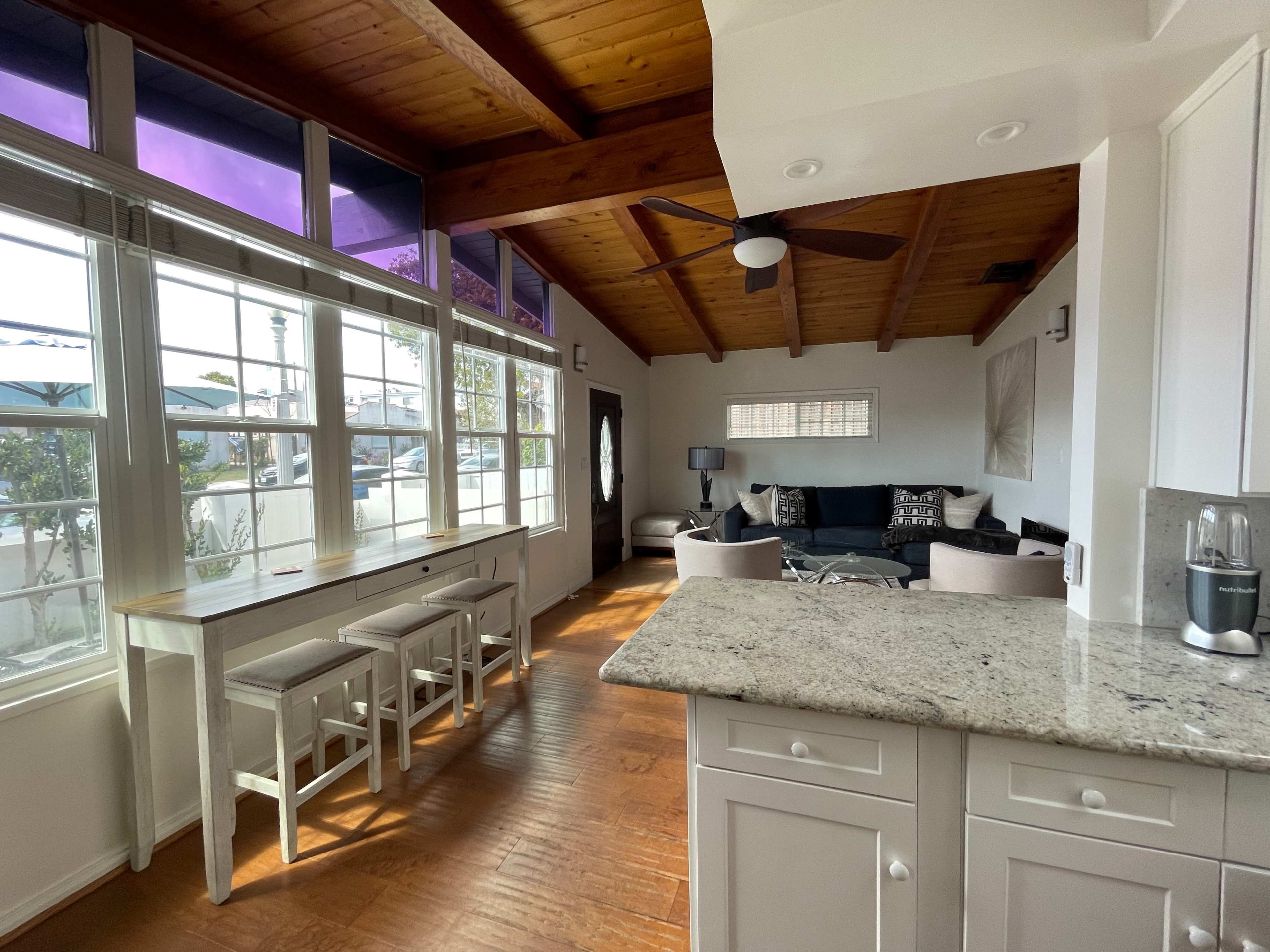 A bright, open-concept living area with a kitchen counter, seating, and large windows providing natural light.