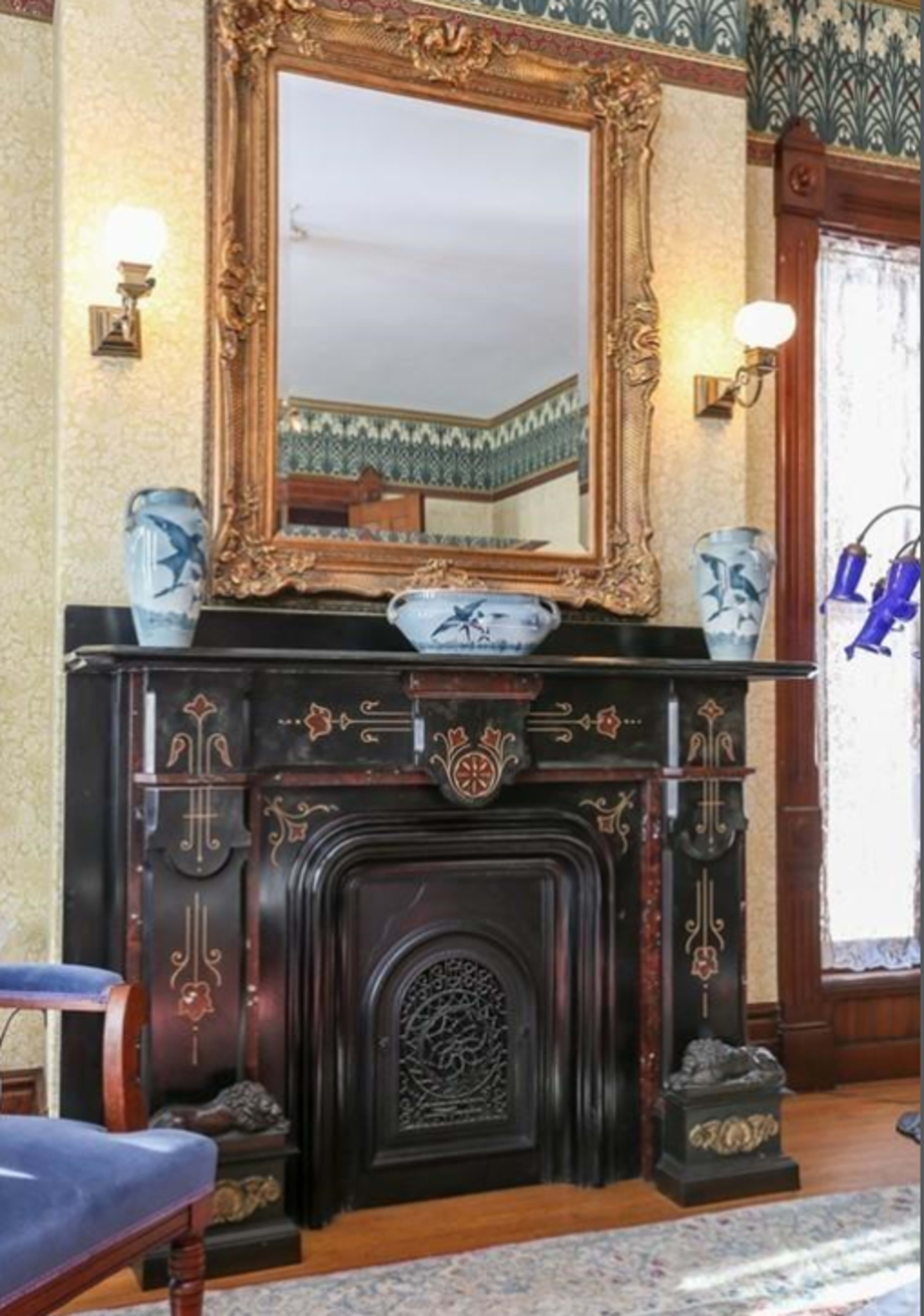 An ornate black fireplace with an intricately designed mantelpiece, flanked by decorative vases and a large, framed mirror above it.