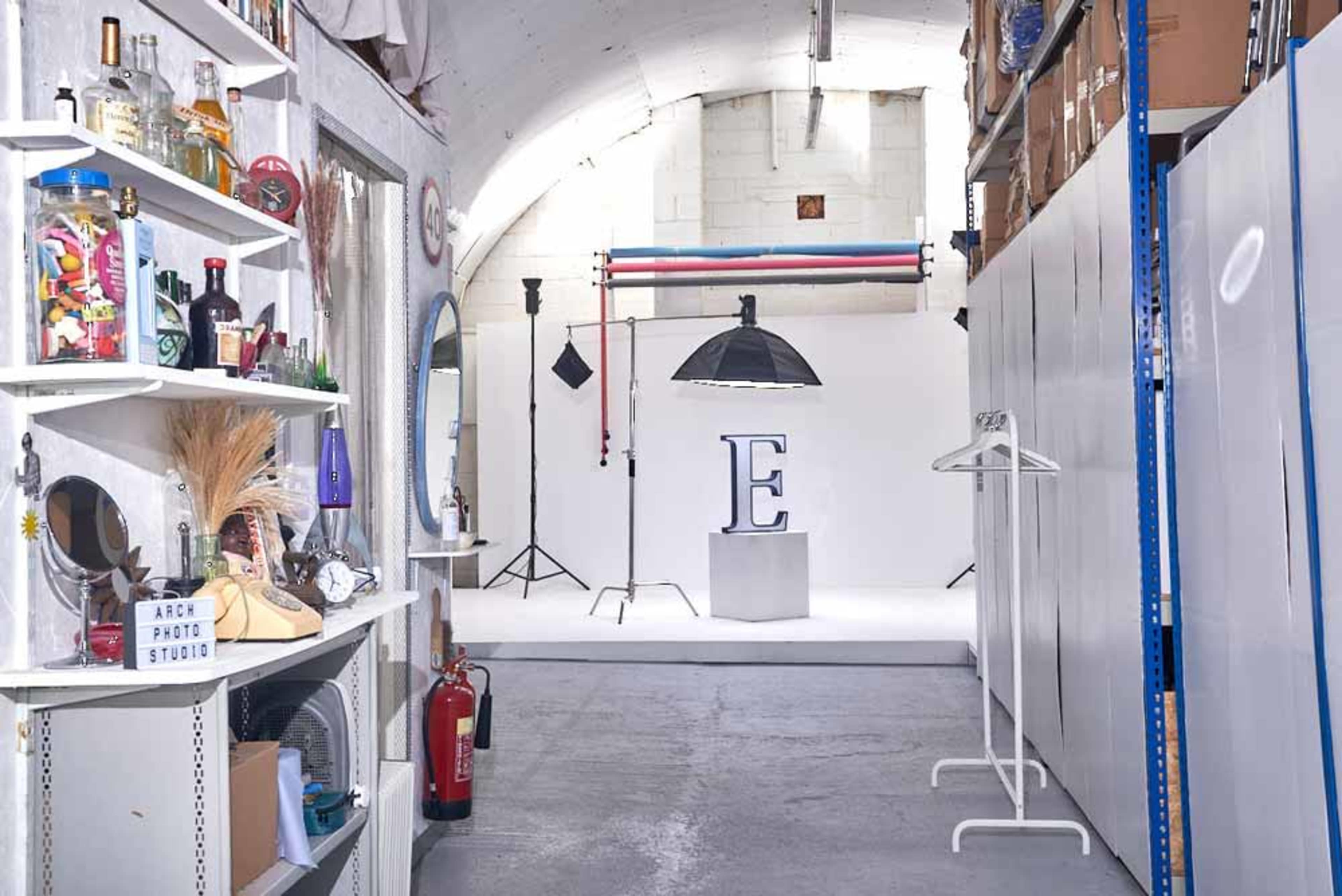 A photography studio with white walls, a central display featuring the letter "E," and various equipment and props arranged along one side.