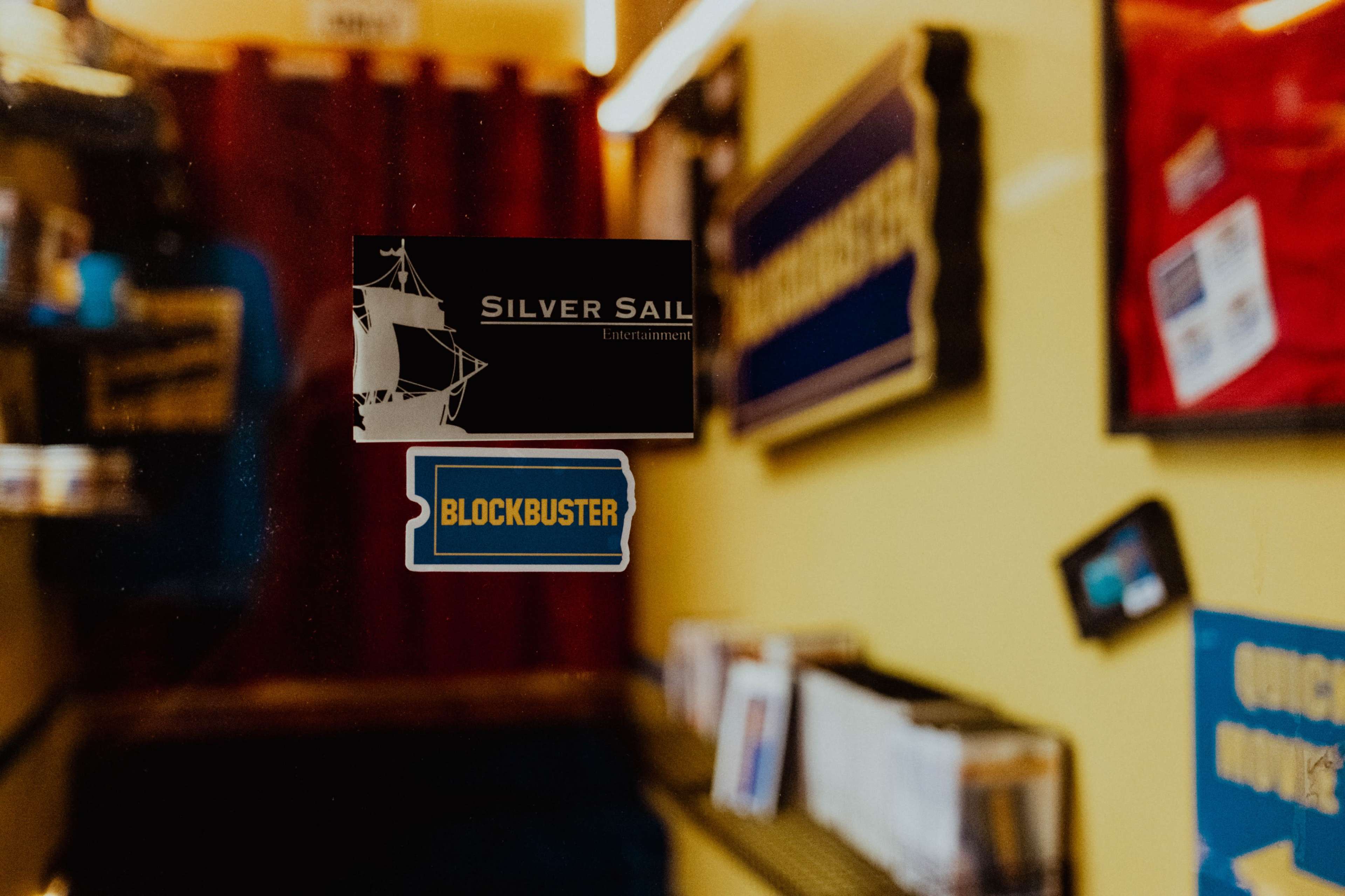 The image shows a storefront window featuring two stickers: one for "Silver Sail Entertainment" and another for "Blockbuster."
