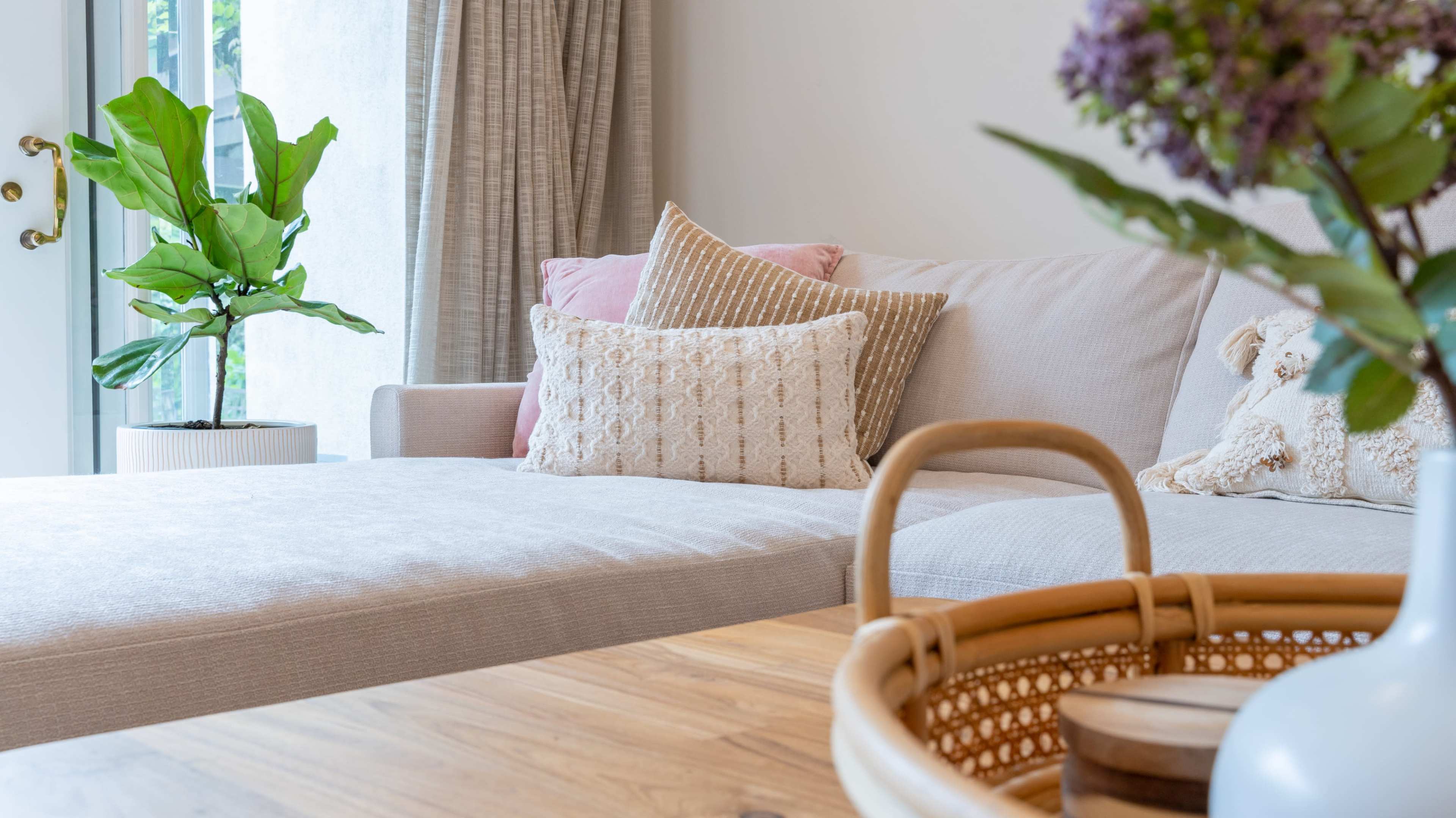 A cozy living room features a light-colored sofa with decorative pillows, a wooden coffee table, and a potted plant by a window.