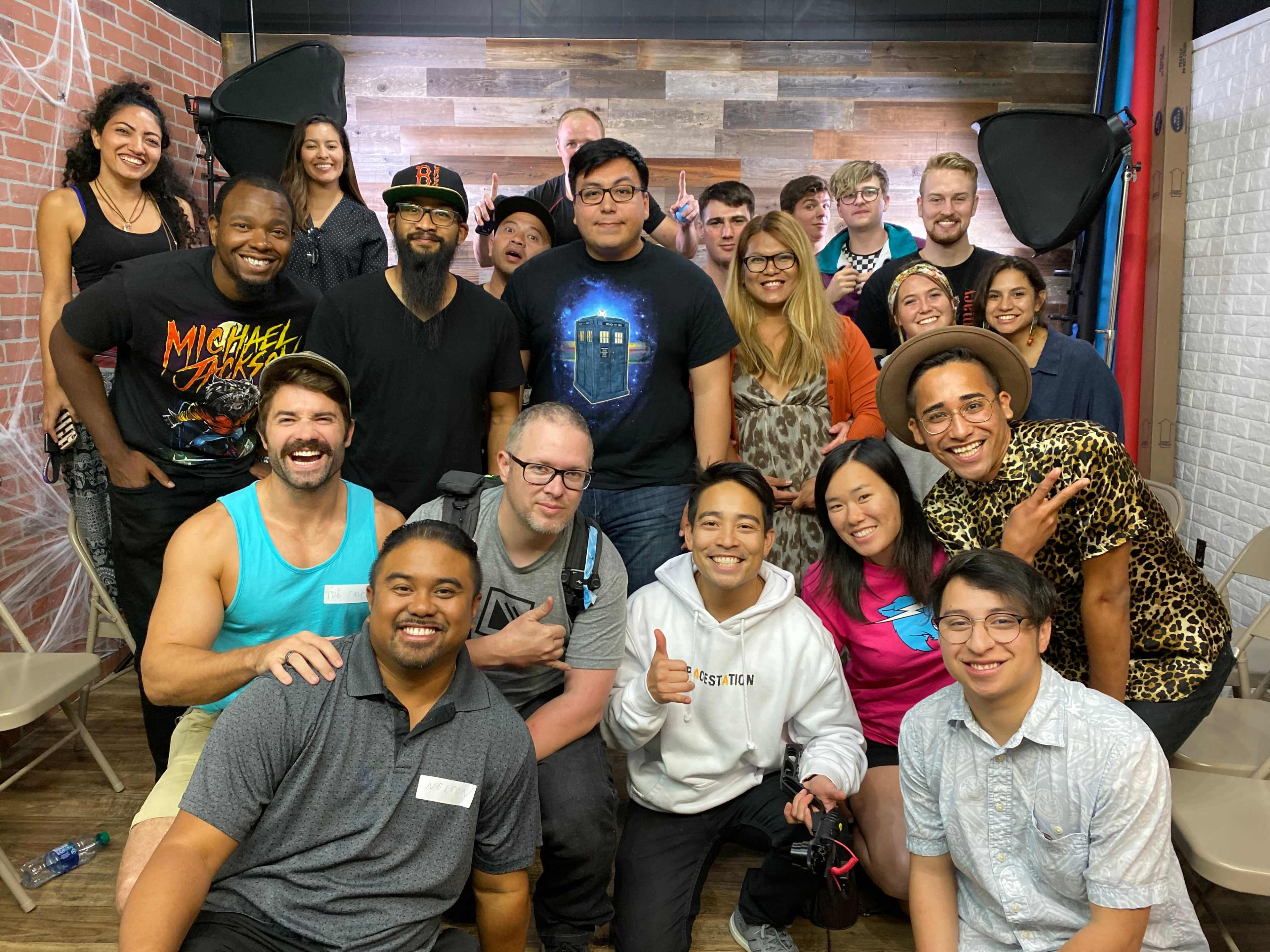 A diverse group of people poses together for a photograph in a studio with wooden walls and studio lighting.