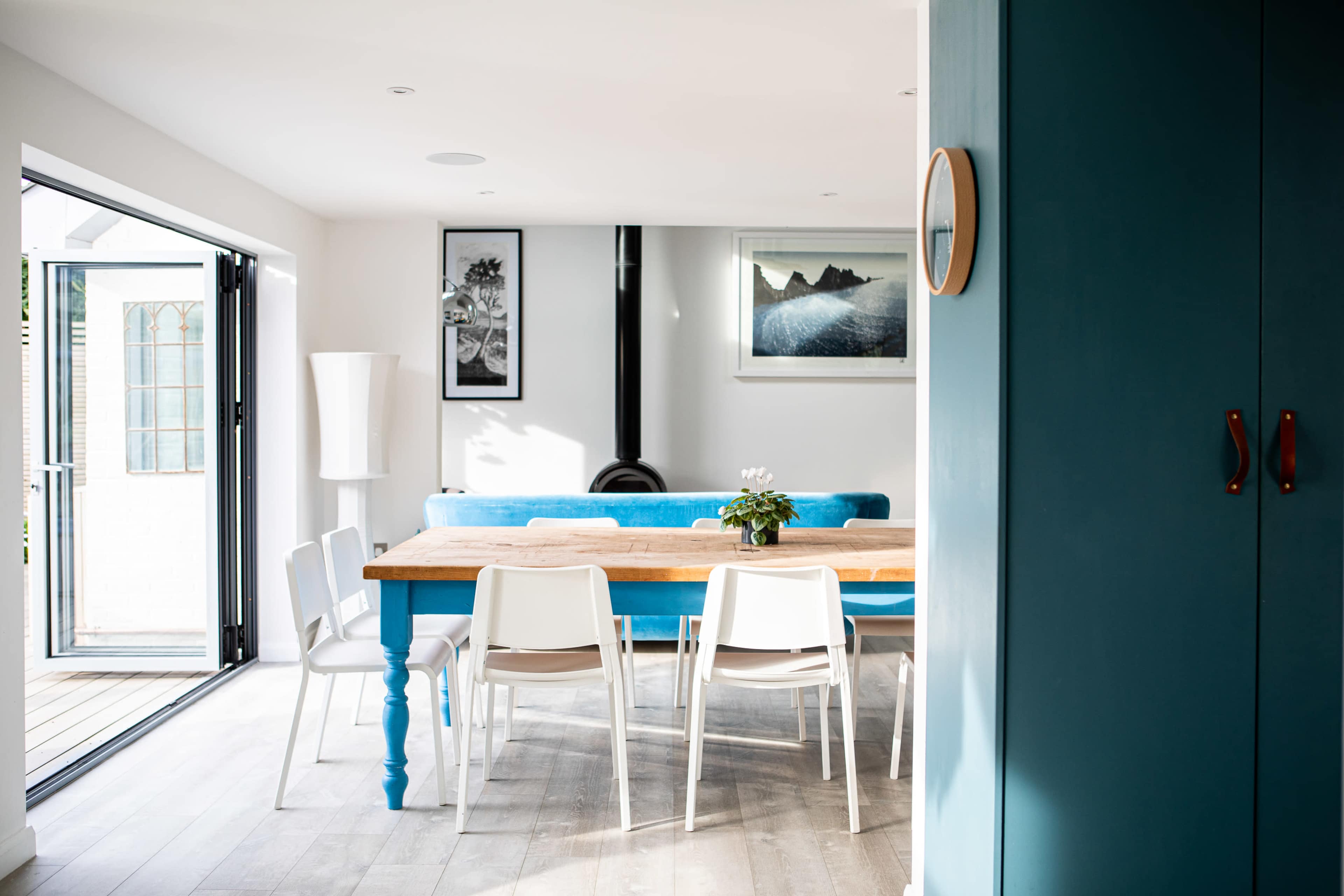 A bright dining area featuring a wooden table surrounded by white chairs, with a blue sofa and large sliding doors leading to an outdoor space.