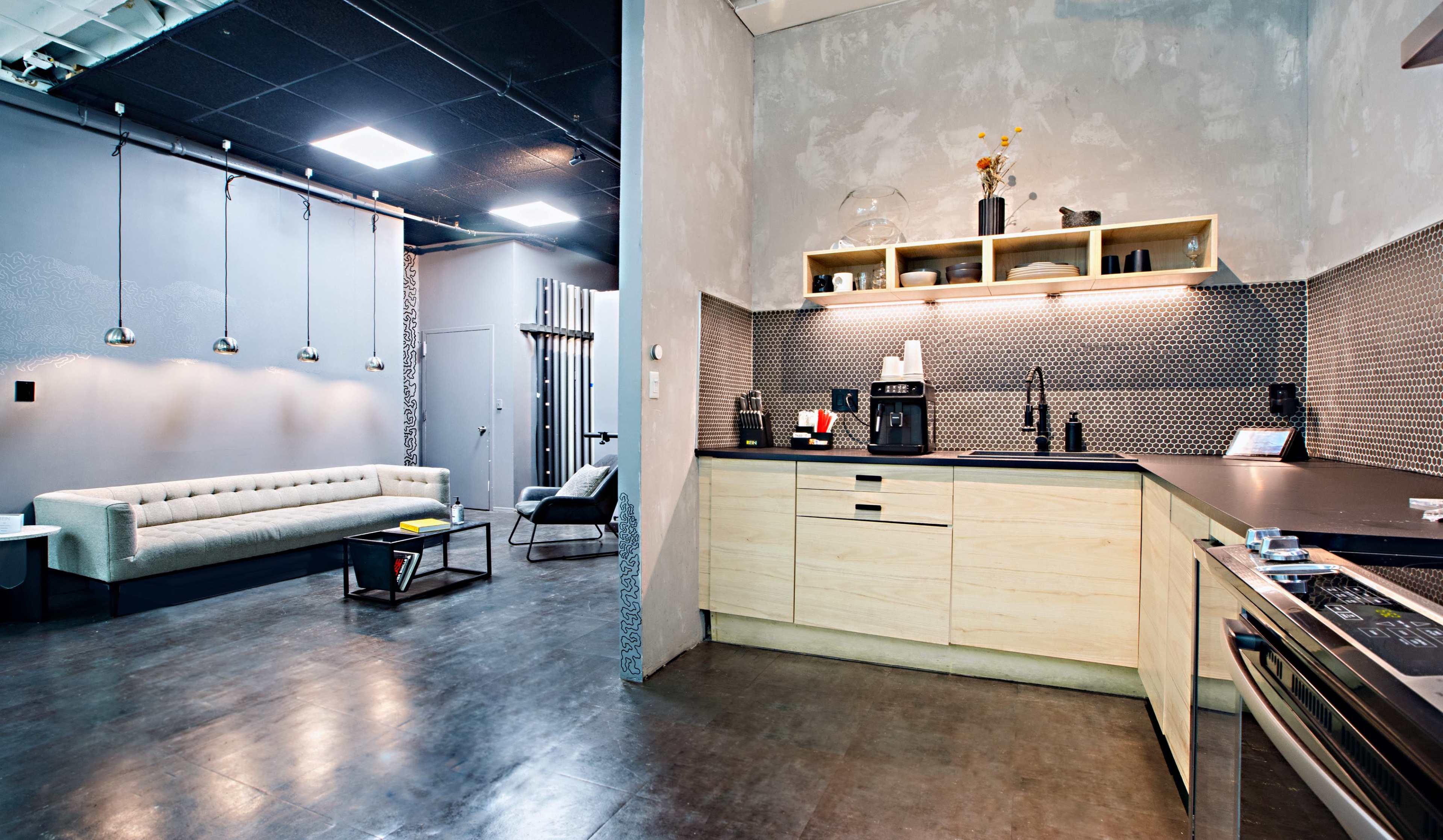 A modern kitchen area with wooden cabinets, a coffee maker, and a gray sofa in a seating area adjacent to it.