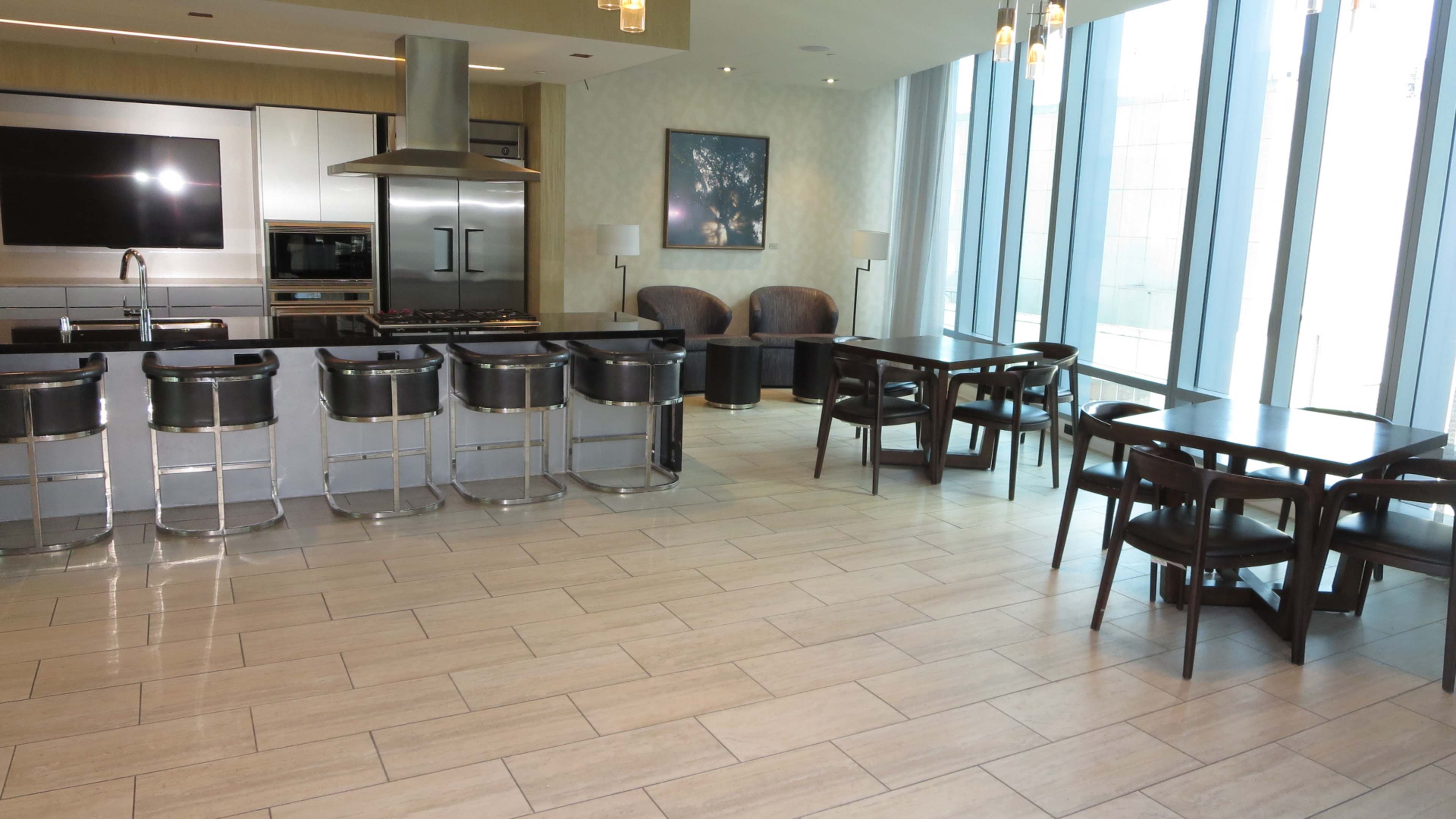 A modern kitchen with a bar counter and stools, a dining area, and large windows allowing natural light to enter the space.