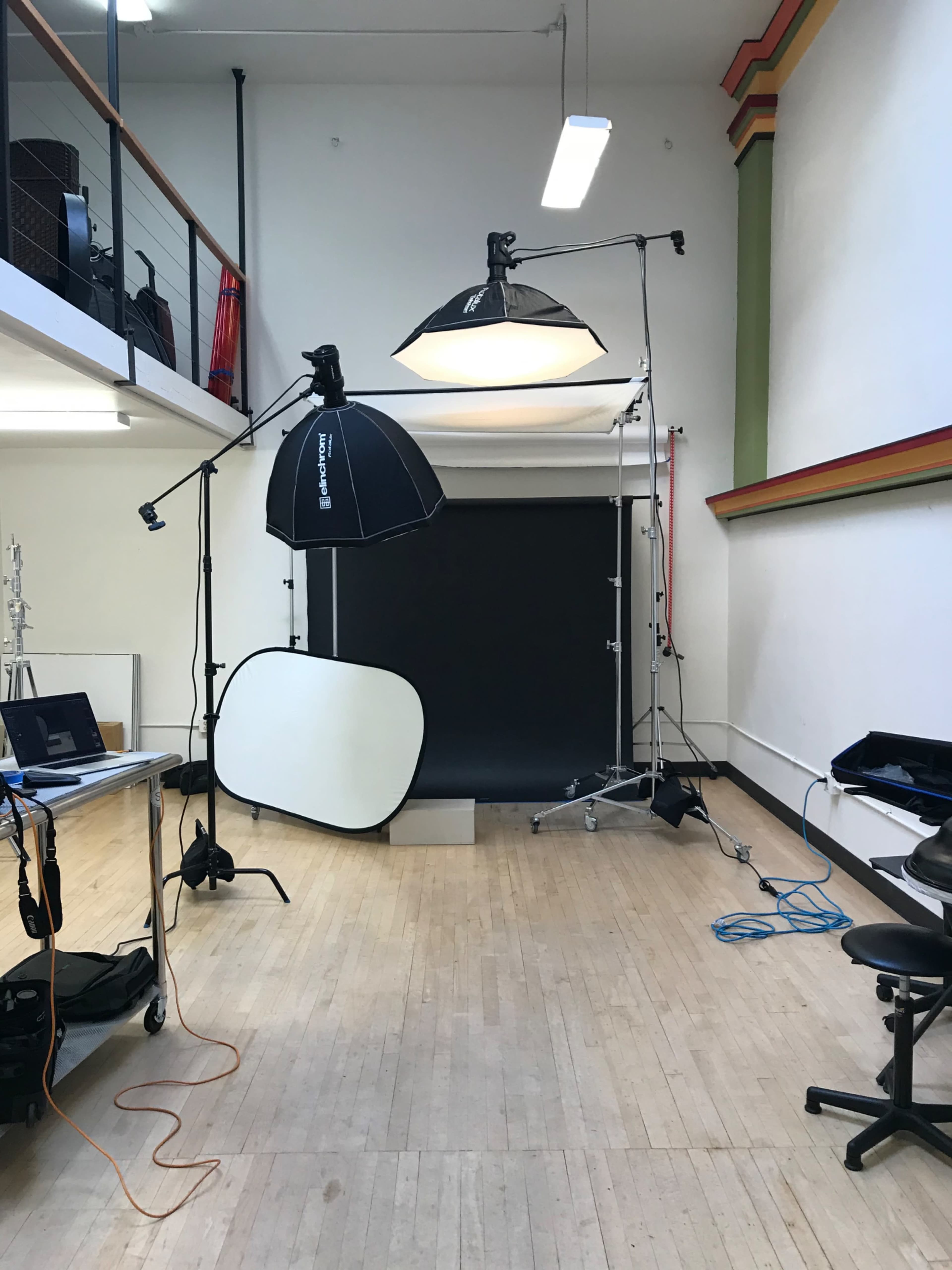 A photography studio is set up with lighting equipment, a dark backdrop, and various props arranged on the floor.