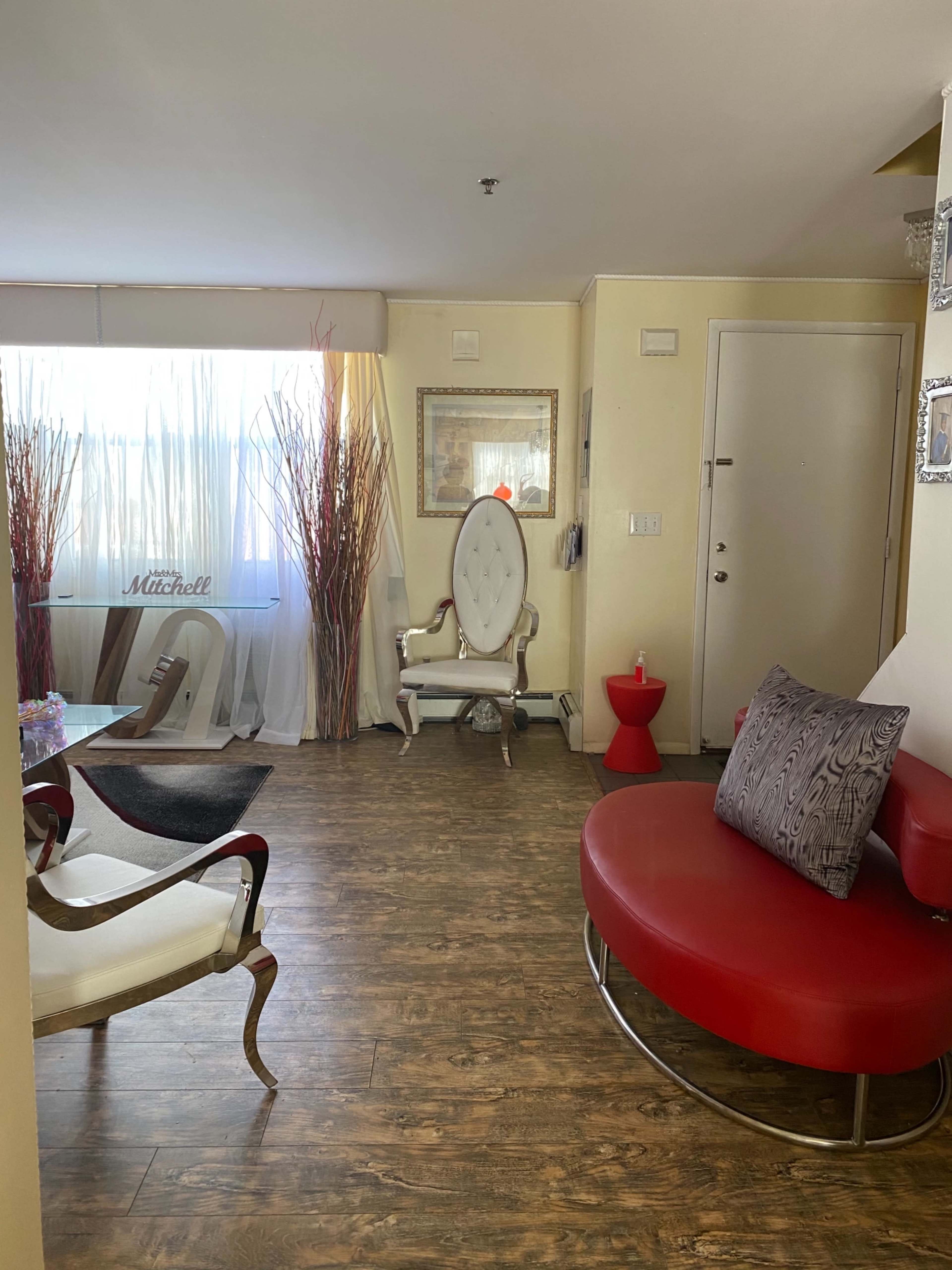 A bright living area featuring modern furniture, including a red circular sofa, a white ornate chair, and decorative plants in tall vases.