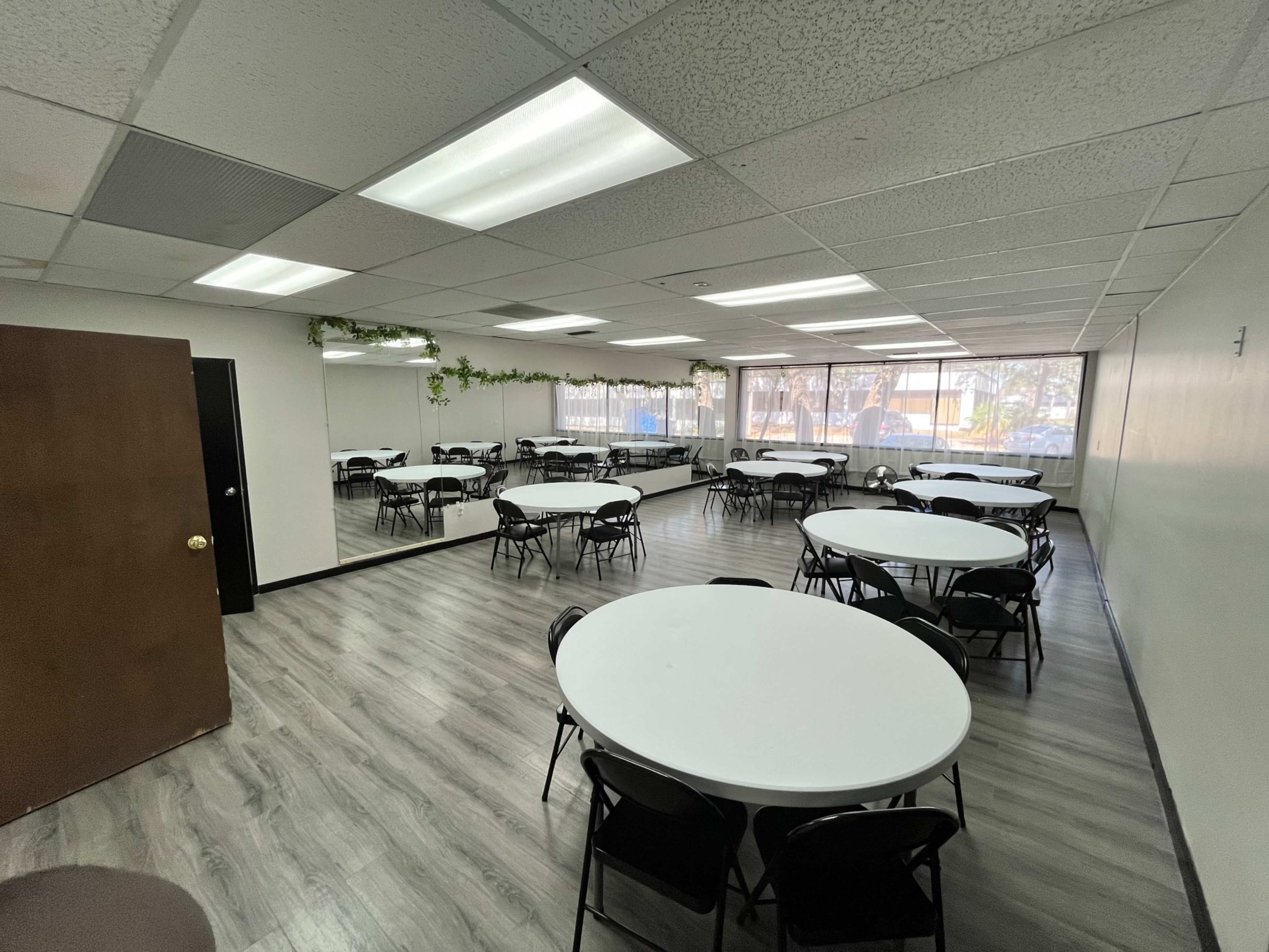 A spacious, brightly lit room with several circular tables and chairs arranged in rows.