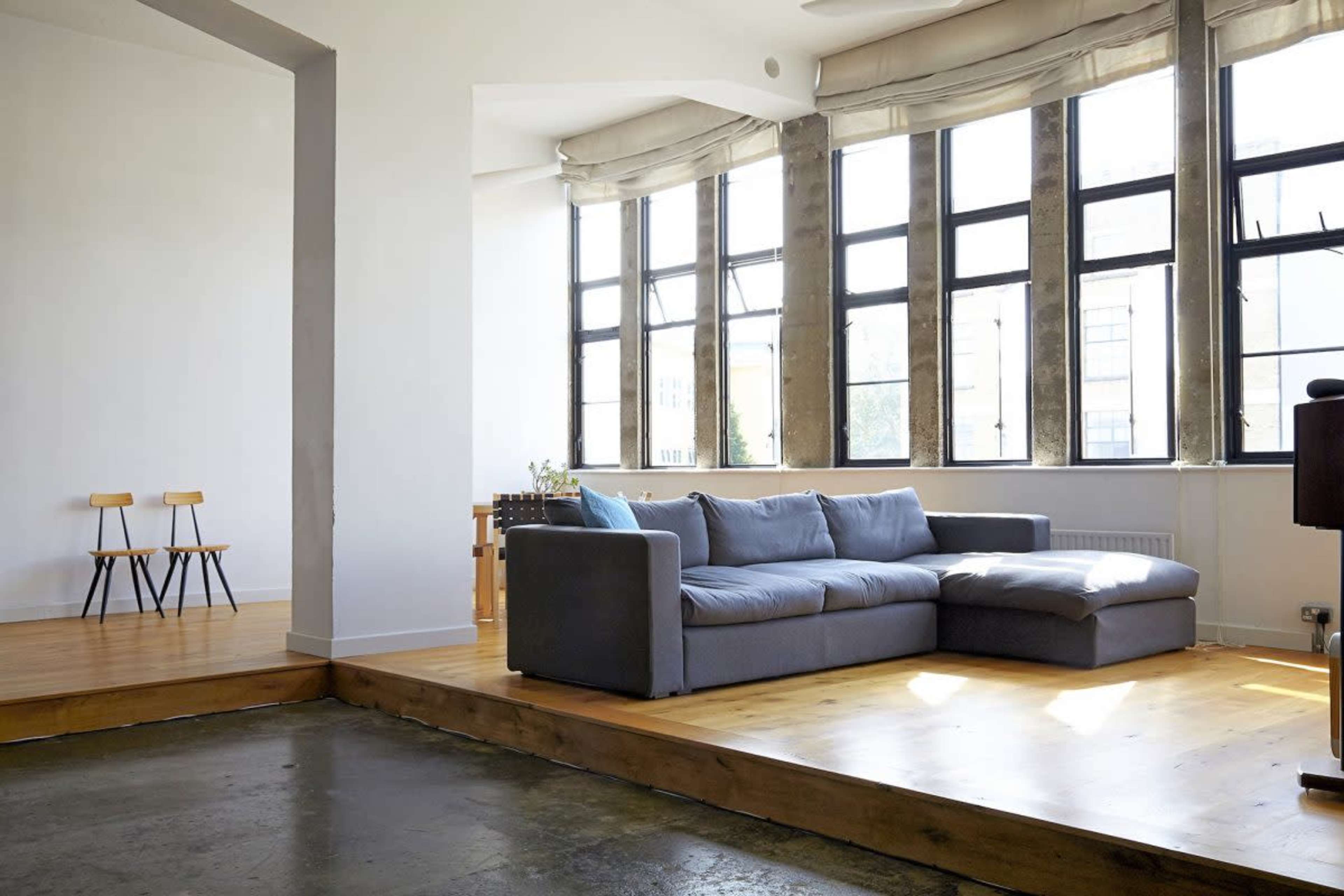 A modern living room features a gray sectional sofa and large windows, with wooden flooring and minimalist furnishings.