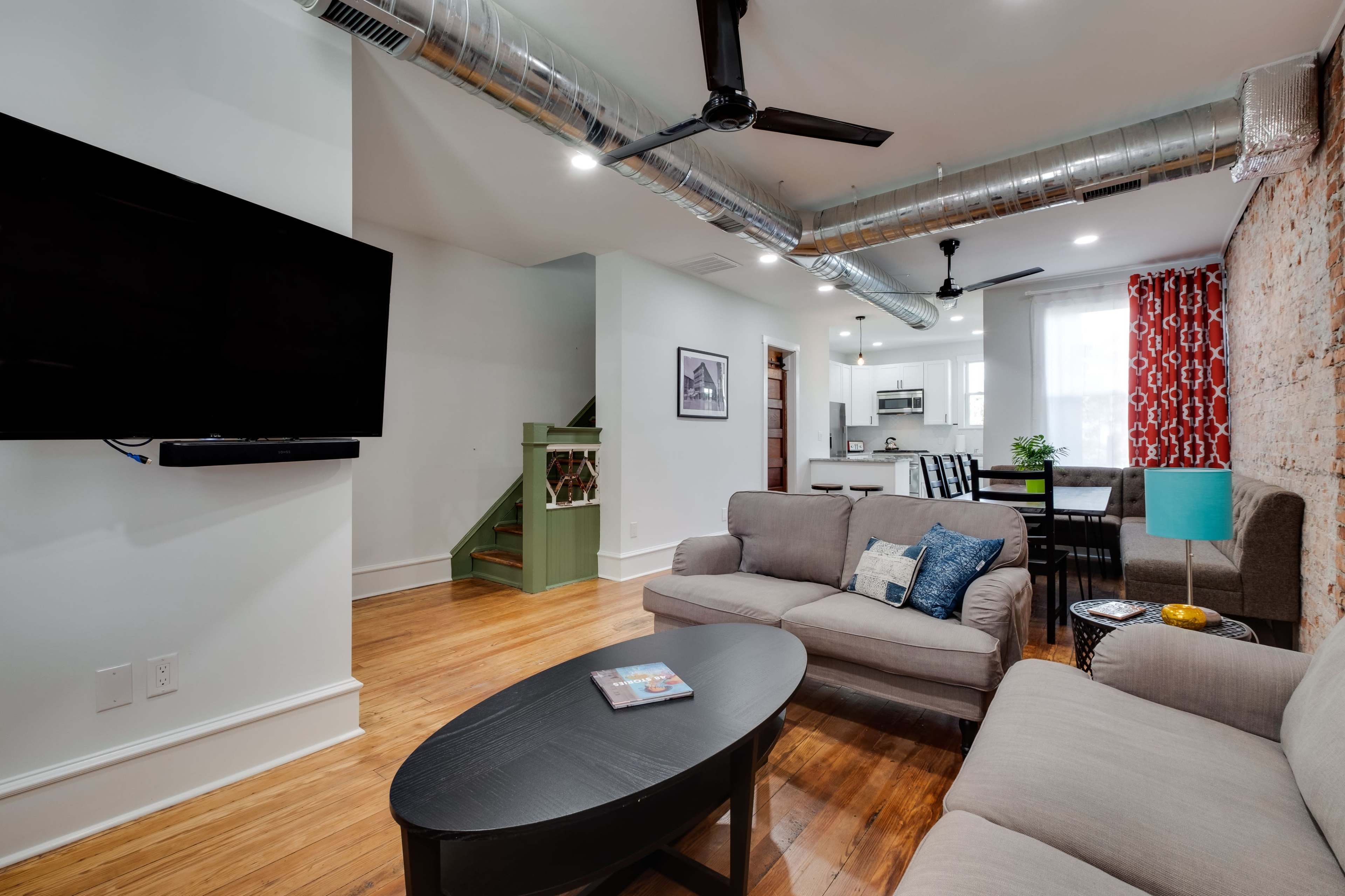 A modern living room with a gray sofa, a round black coffee table, and an exposed brick wall, leading to a kitchen area in the background.