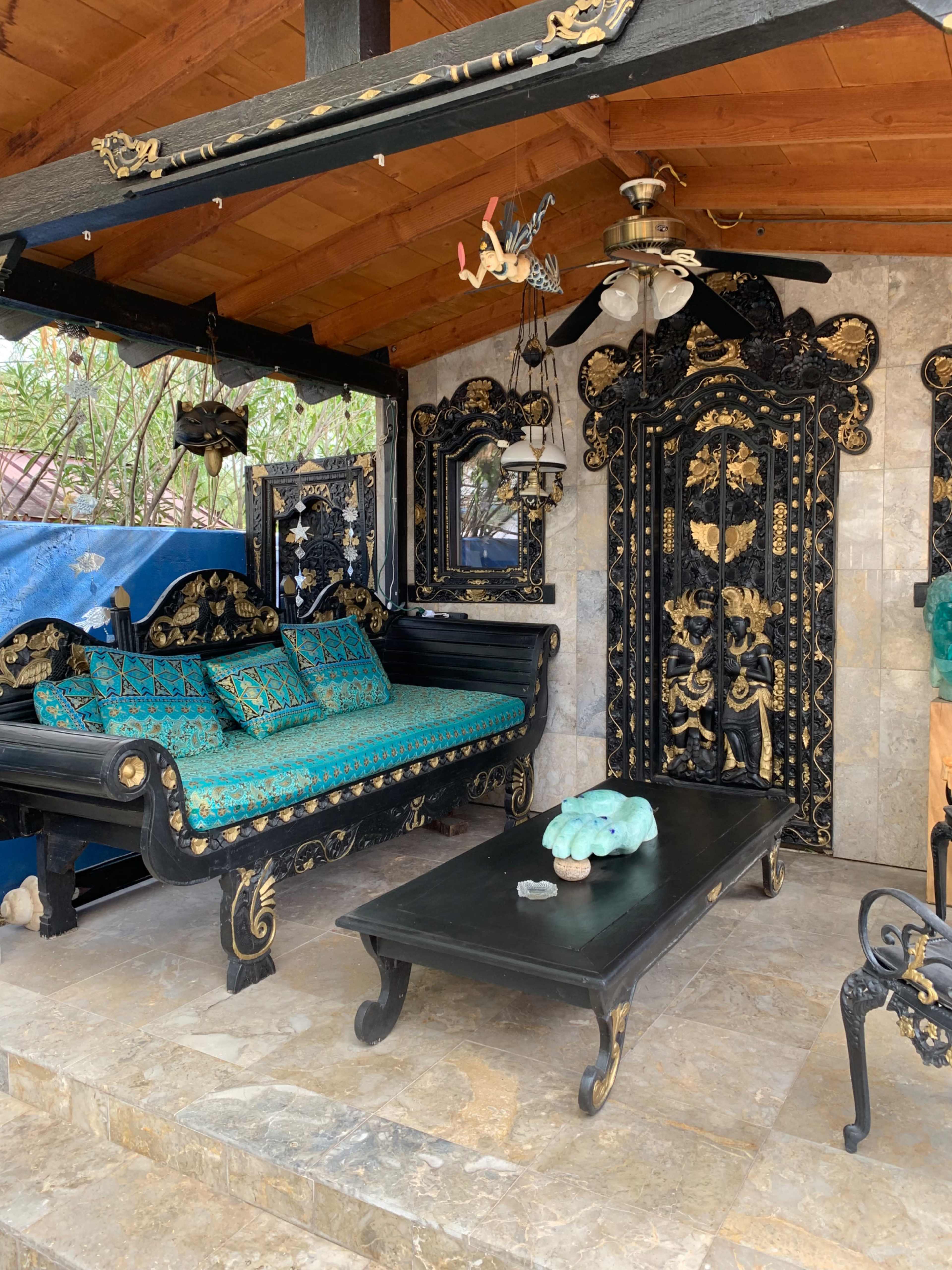 A decorated outdoor seating area featuring a black wooden sofa with turquoise cushions, a matching coffee table, and ornate wall decor.