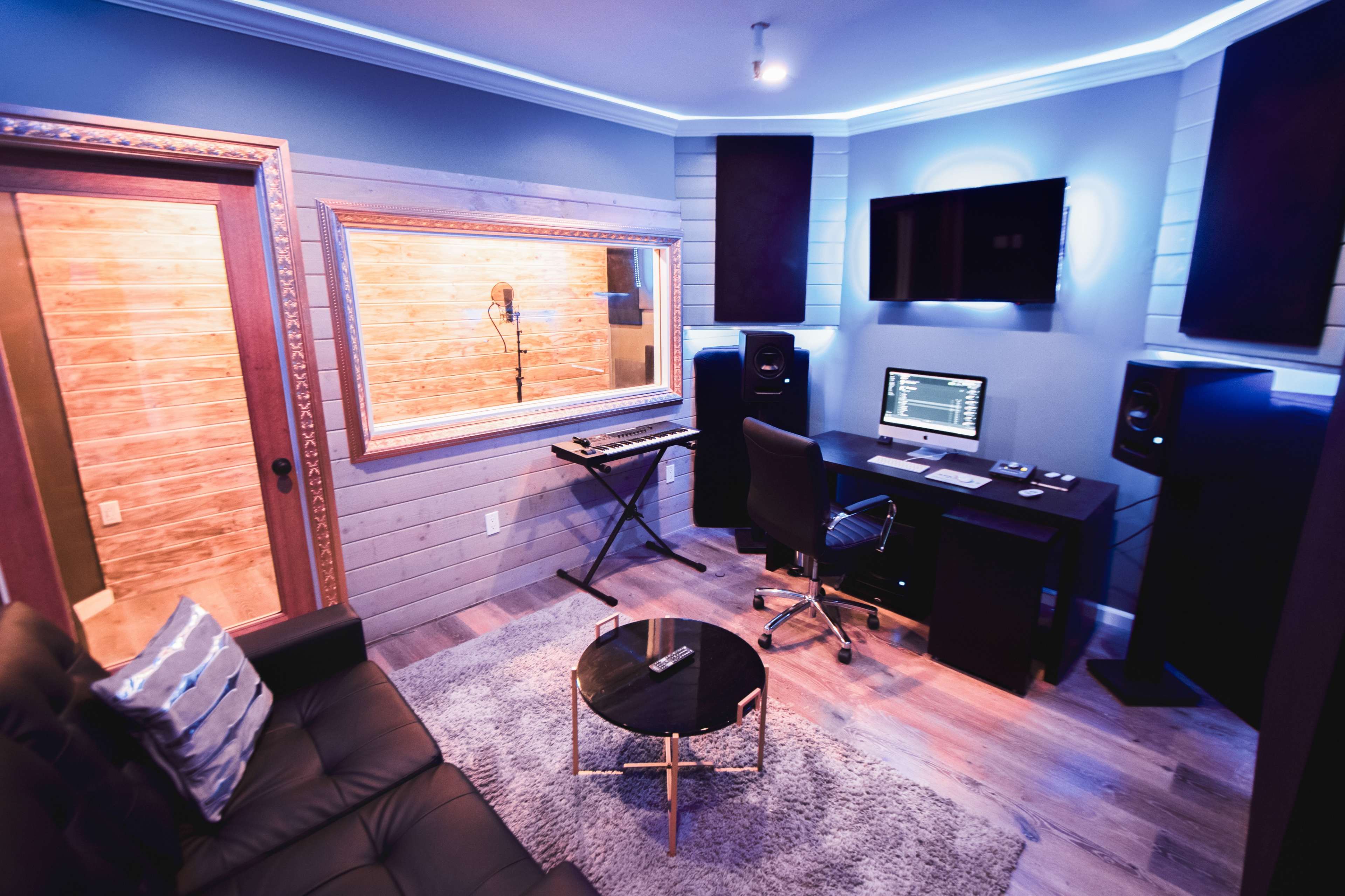 A modern recording studio with a control desk, speakers, a microphone booth, and a comfortable seating area.