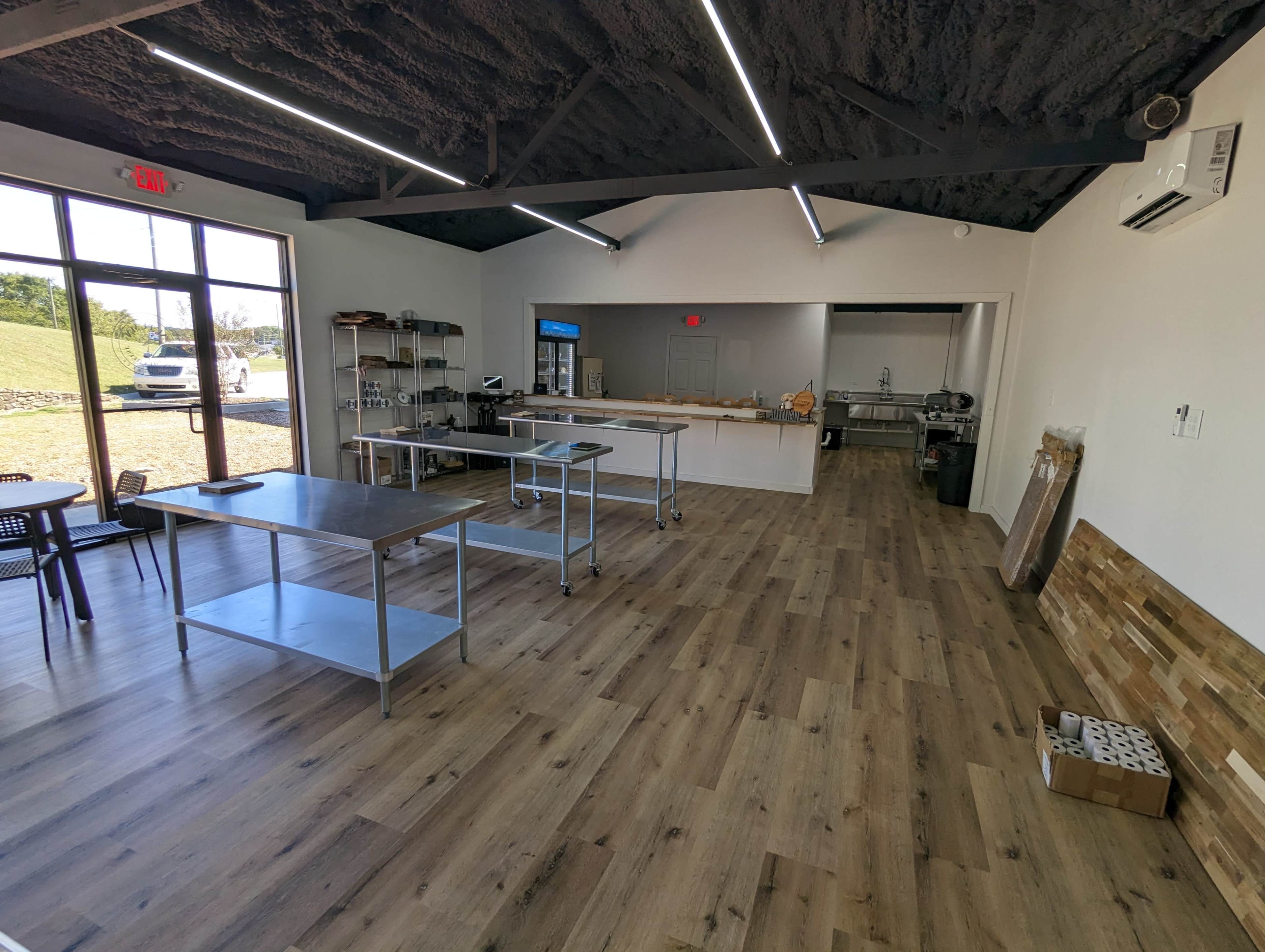 A spacious, modern interior of a commercial kitchen with stainless steel tables, equipment, and a large open area featuring wooden flooring and a ceiling with visible beams.