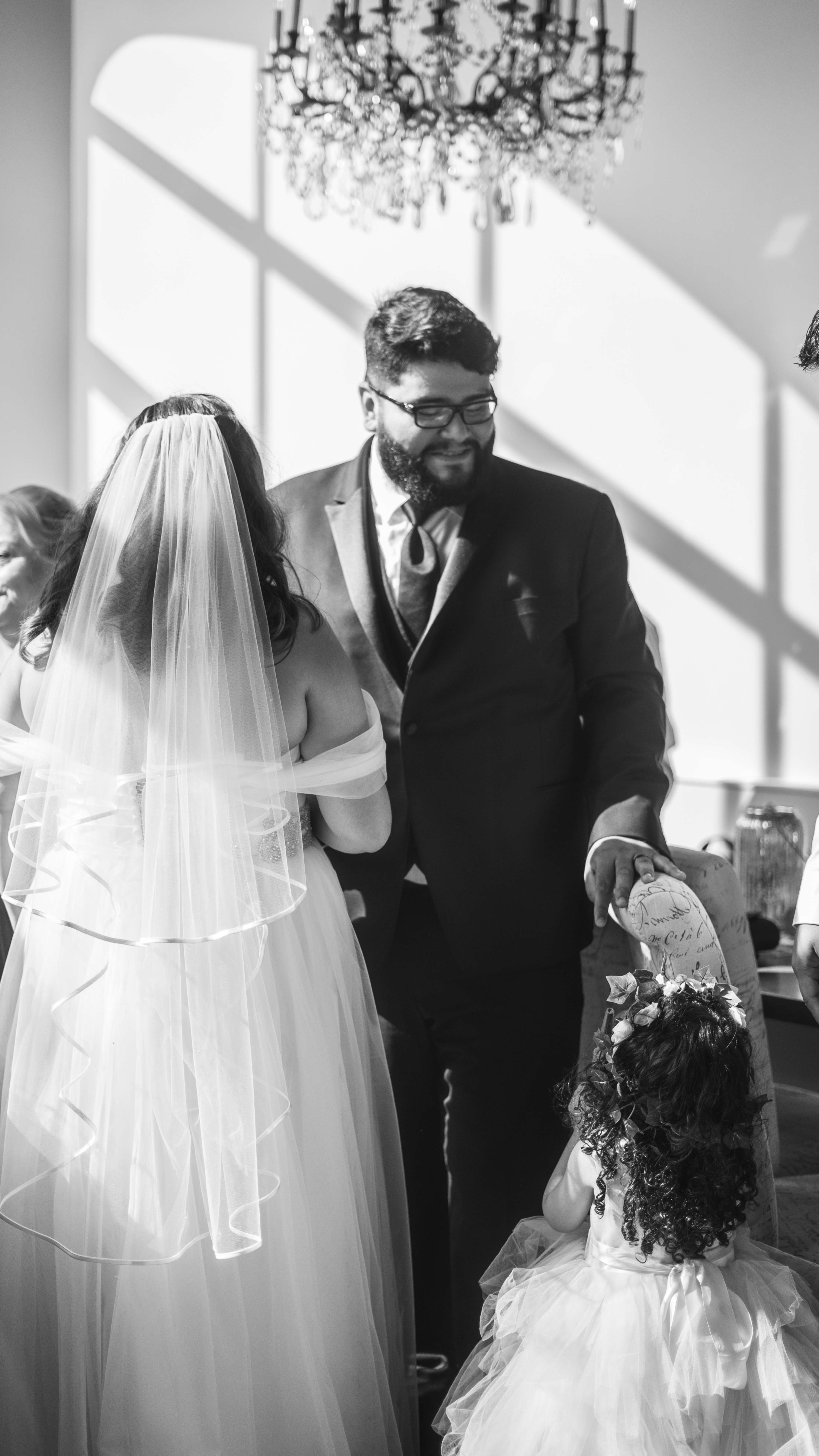 A man in a suit stands next to a woman in a wedding dress, while a child in a sparkling dress looks up at them.