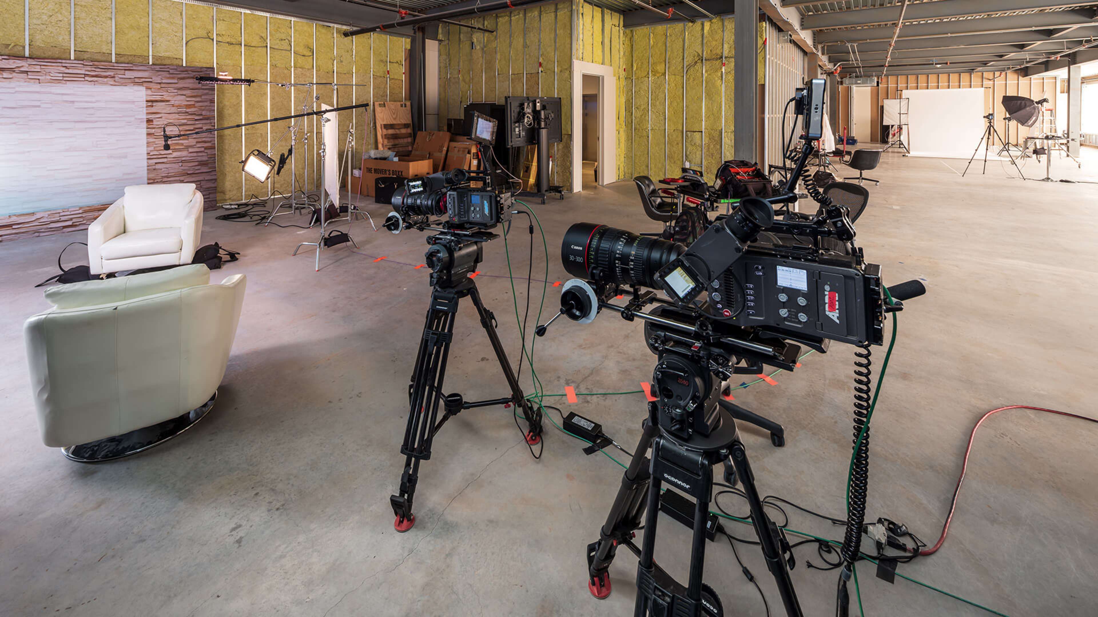 A spacious studio setup with two professional cameras facing a white chair against a textured backdrop.