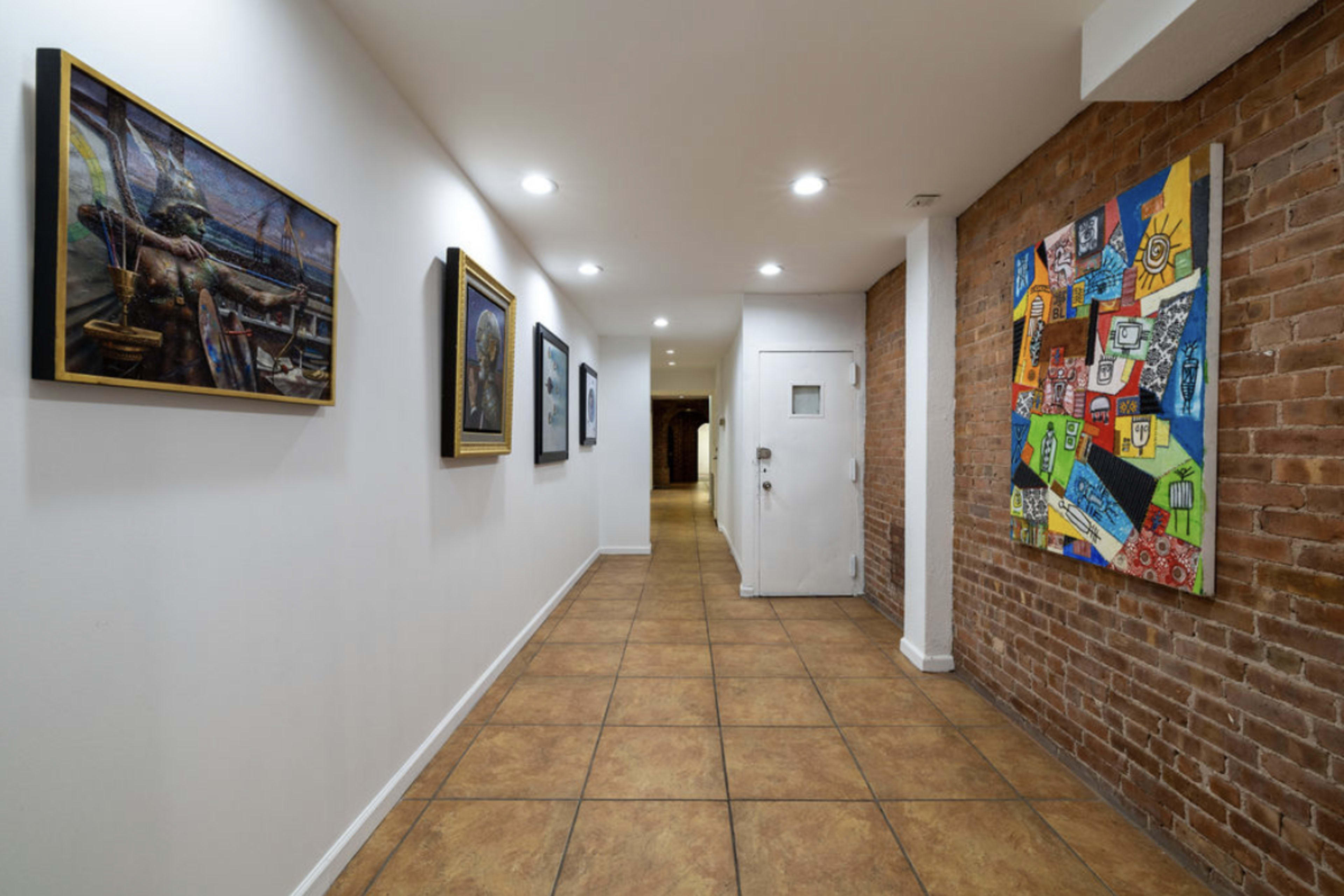 A hallway with brick walls, tiled flooring, and several framed artworks displayed along one side.
