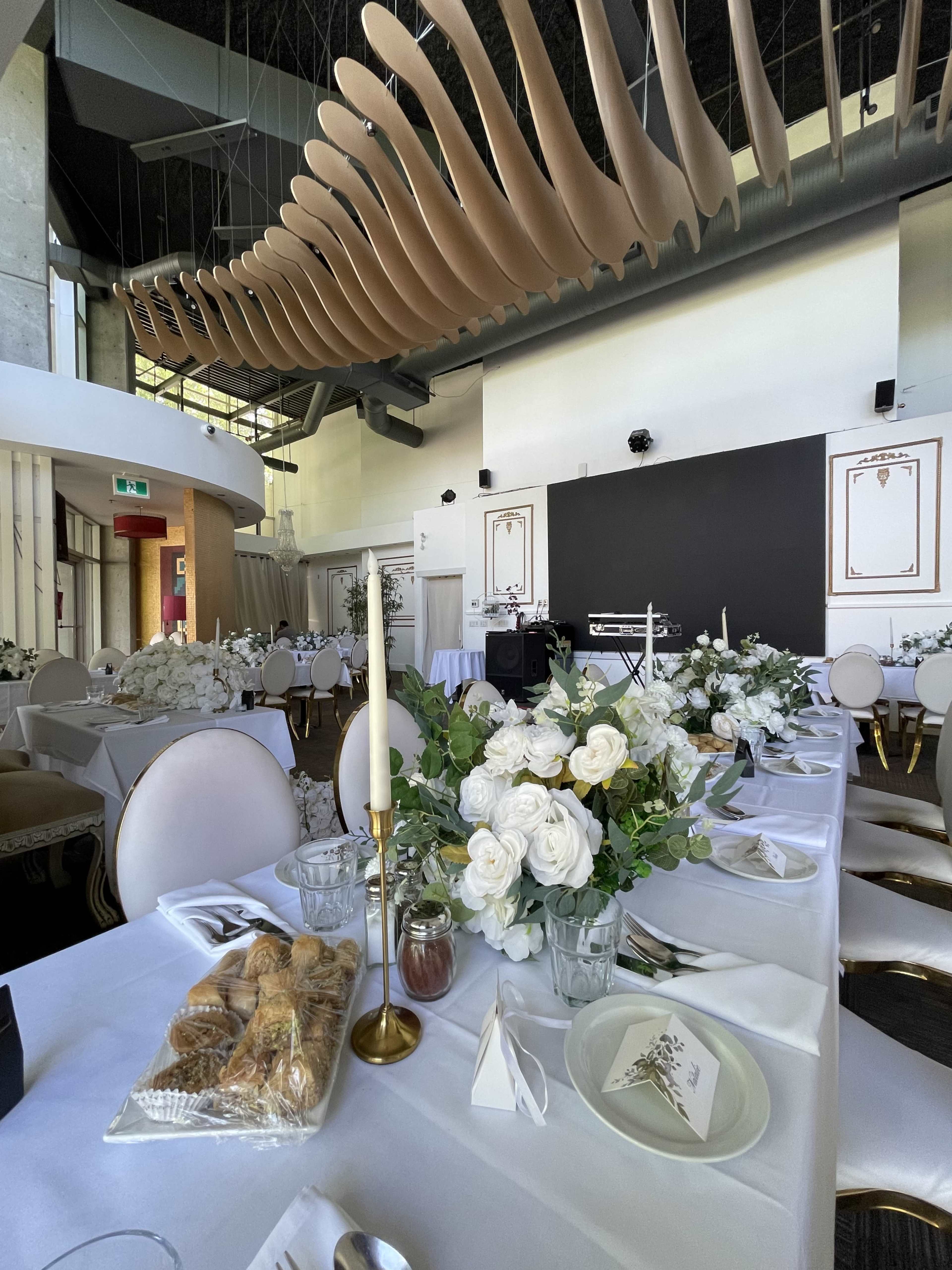 The image shows a elegantly set dining table in a modern venue adorned with white floral arrangements, candles, and pastries.