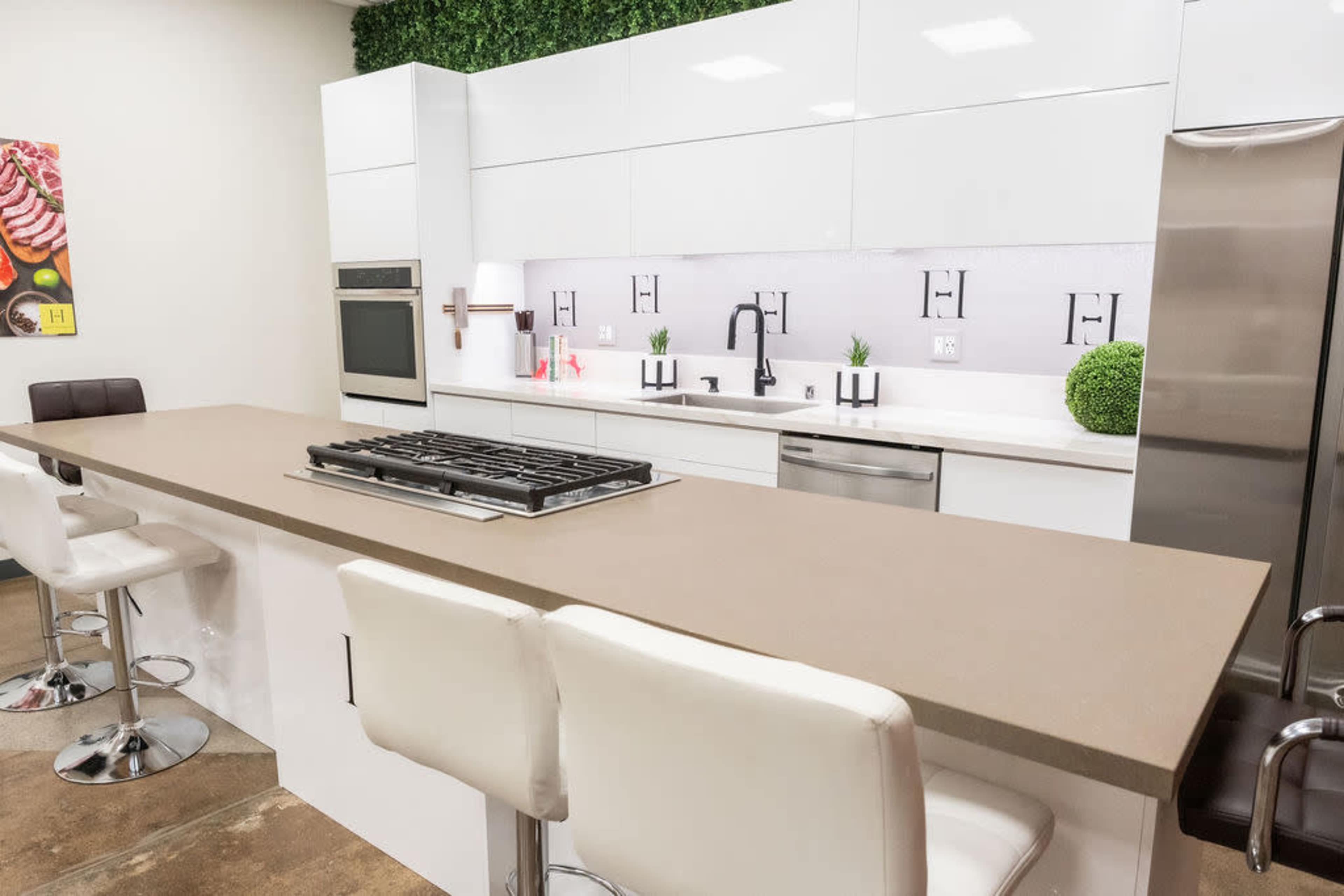The image shows a modern kitchen with white cabinetry, a central island with a built-in stovetop, and bar stools.