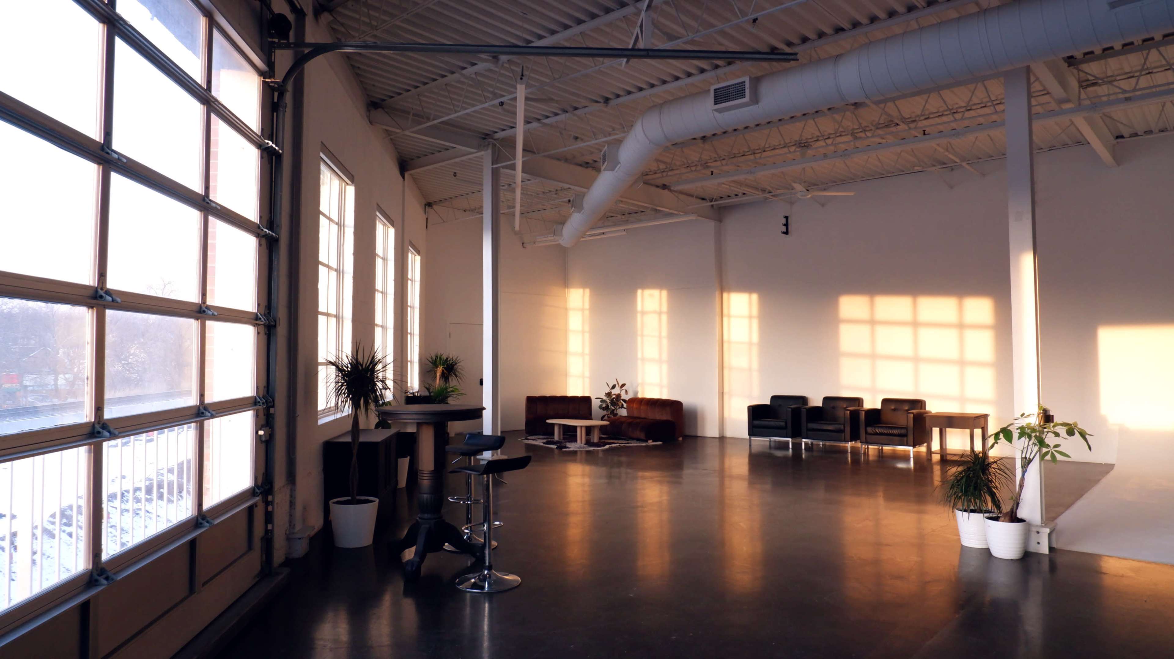 A spacious interior with large windows, polished concrete flooring, and a seating area featuring dark chairs and a small table.