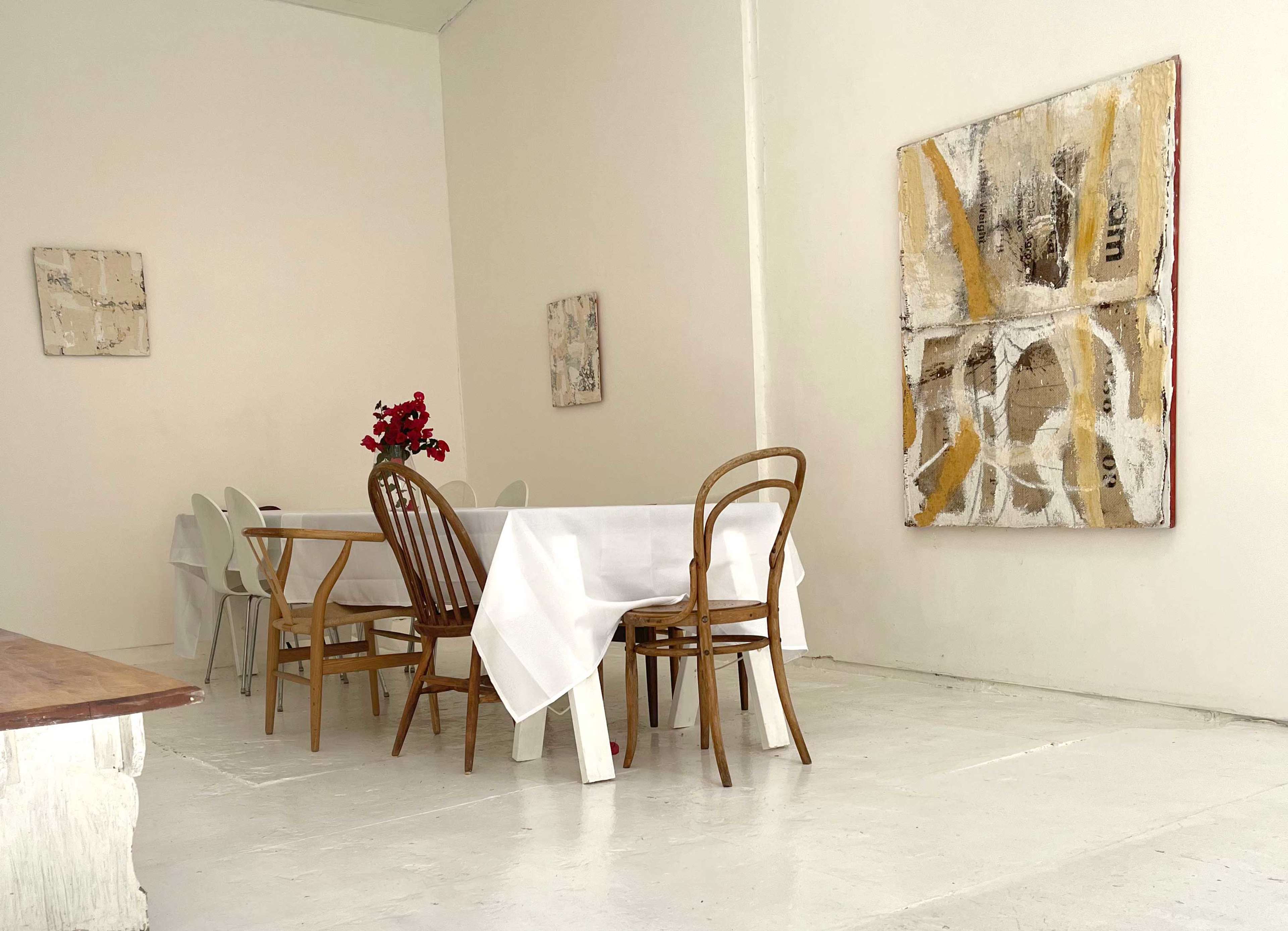 A minimalist dining space features a white table with chairs, adorned by a floral centerpiece and accompanied by abstract artwork on the walls.