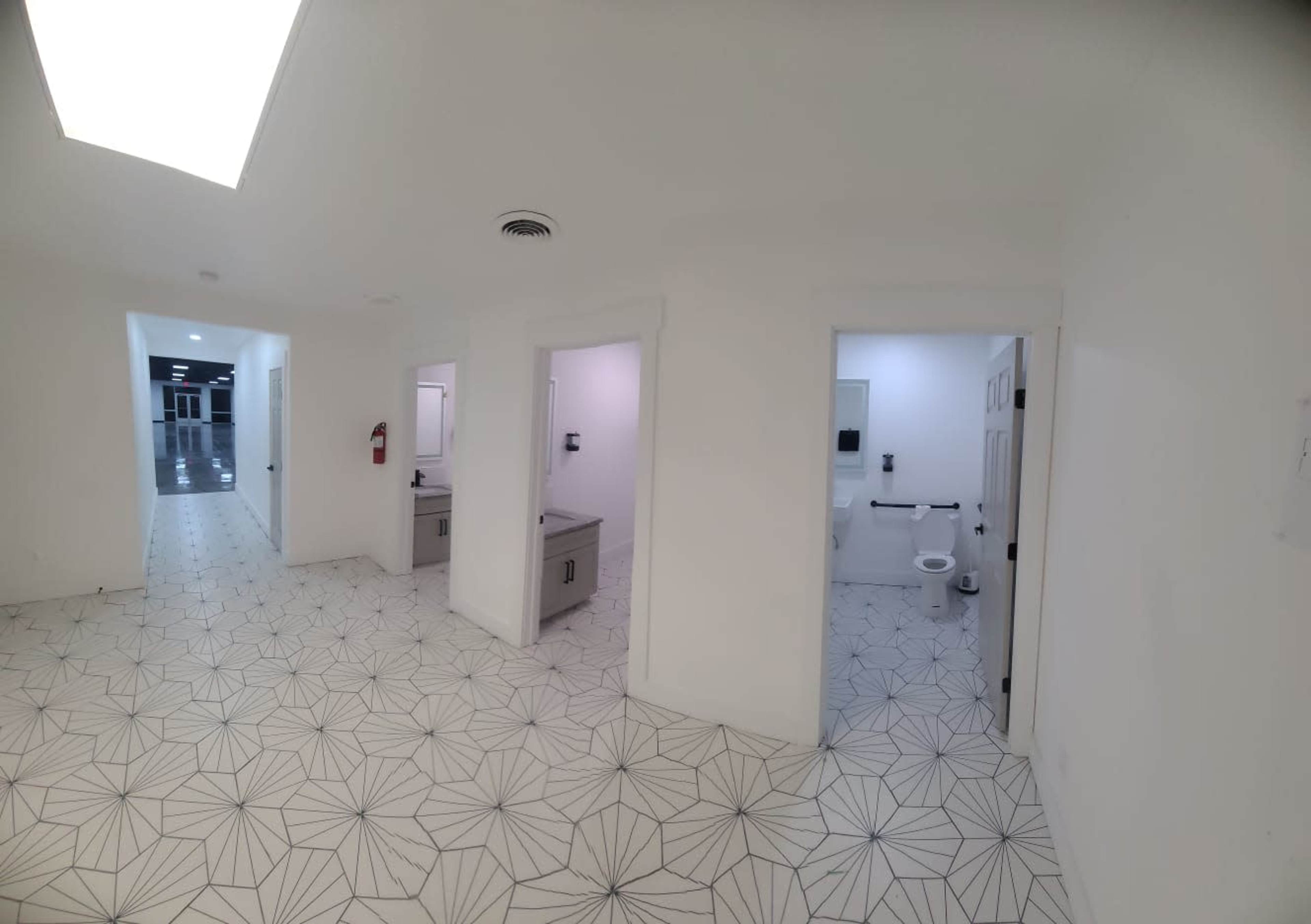 A light-filled corridor with white walls, a patterned floor, and three entrances to restrooms or utility rooms.