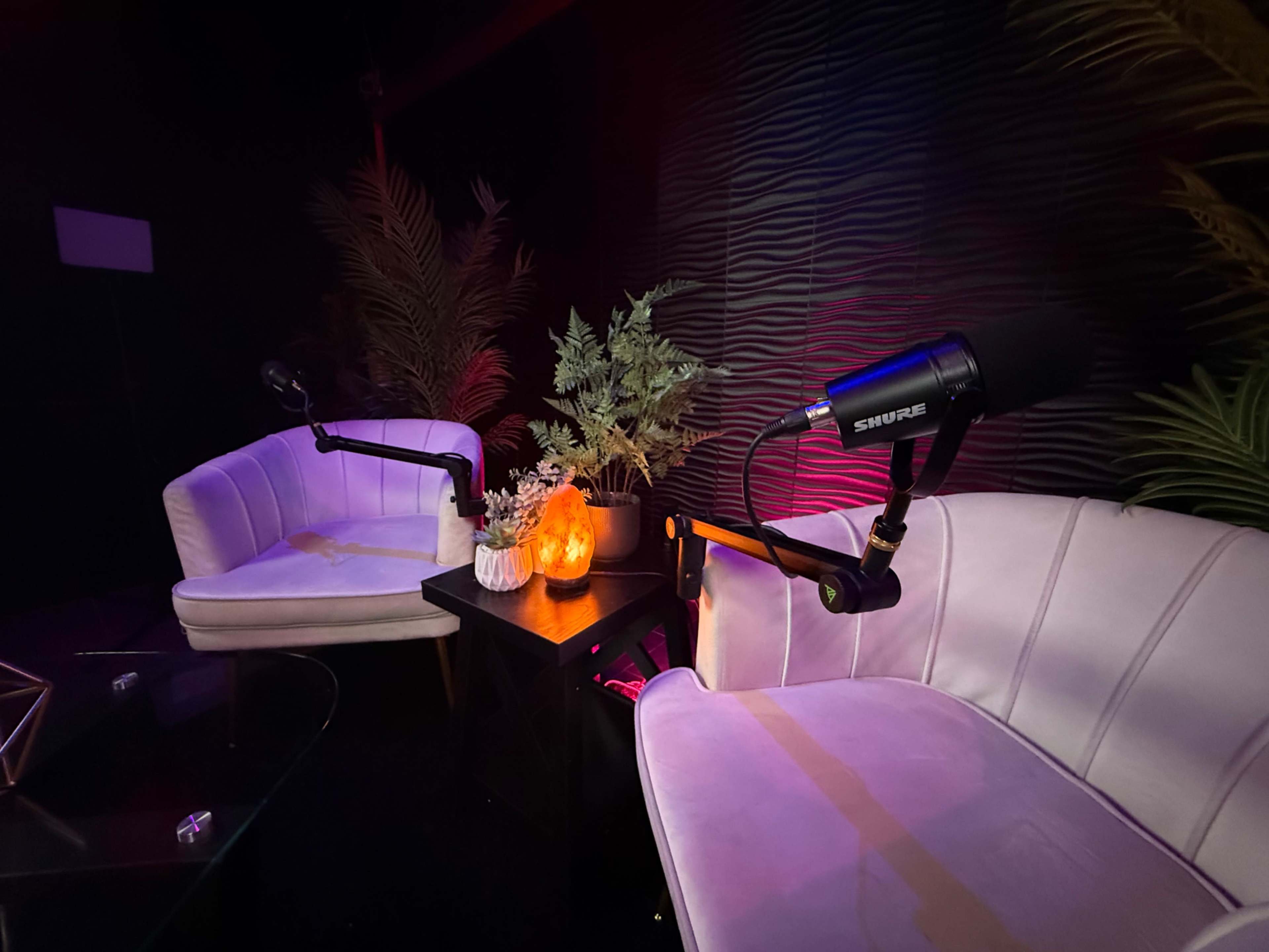 The image shows two white chairs positioned beside a small table with a decorative pumpkin and microphone, set against a textured, dark wall with ambient lighting.