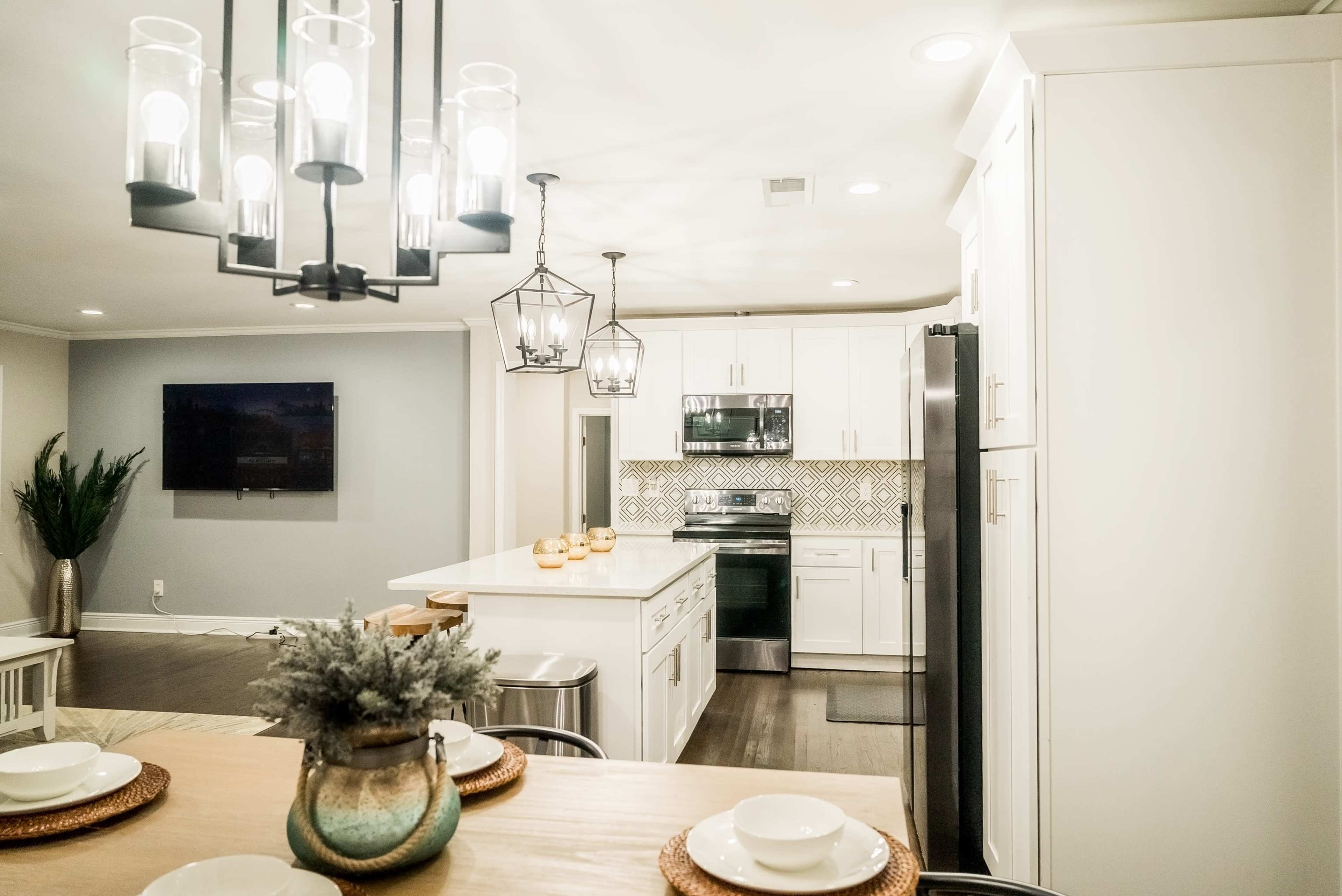 A modern kitchen with white cabinets, stainless steel appliances, and a dining area featuring a wooden table set for a meal.