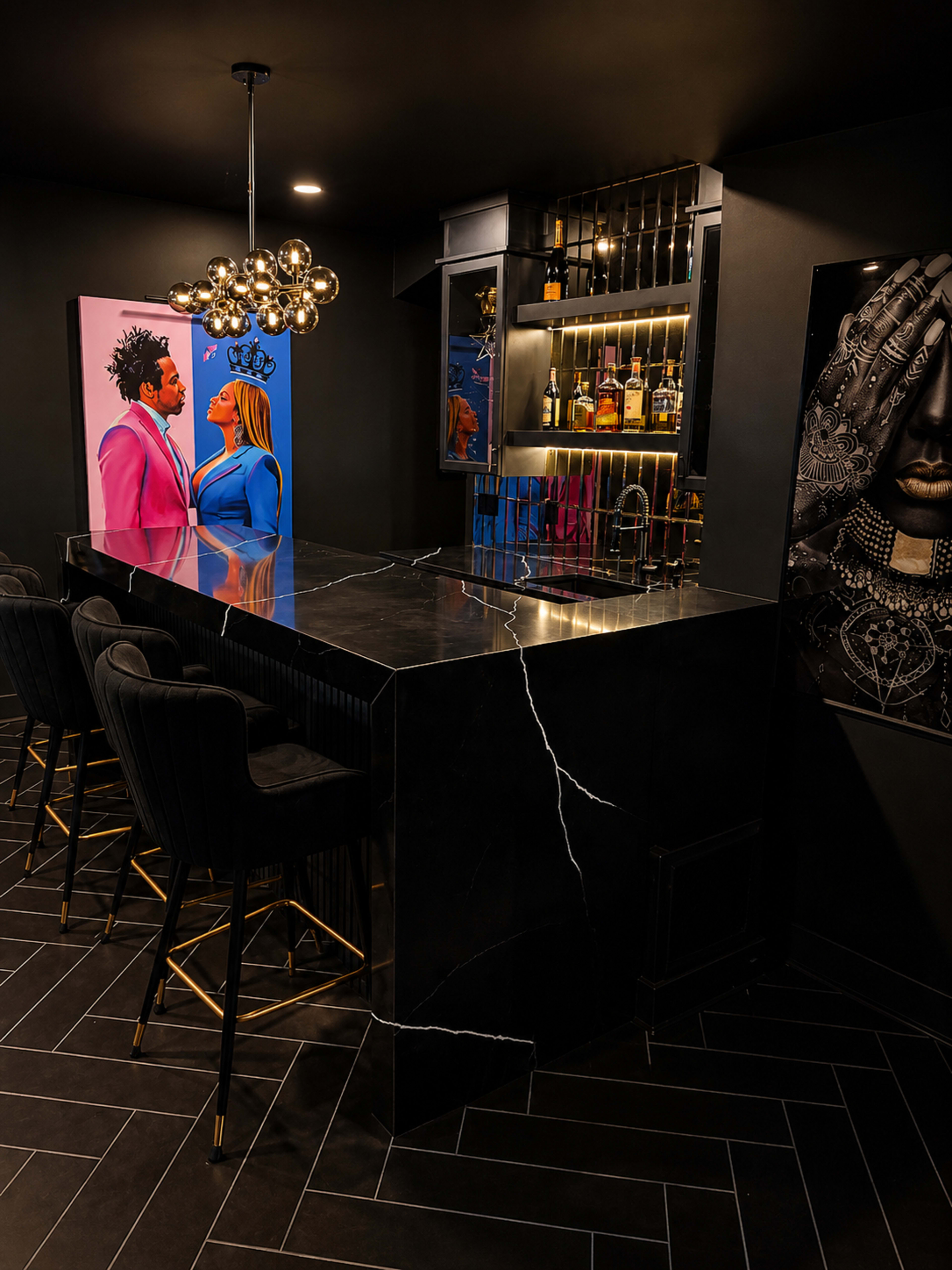 The image shows a modern home bar featuring a black marble countertop, stylish black bar stools, and colorful artwork on the walls.