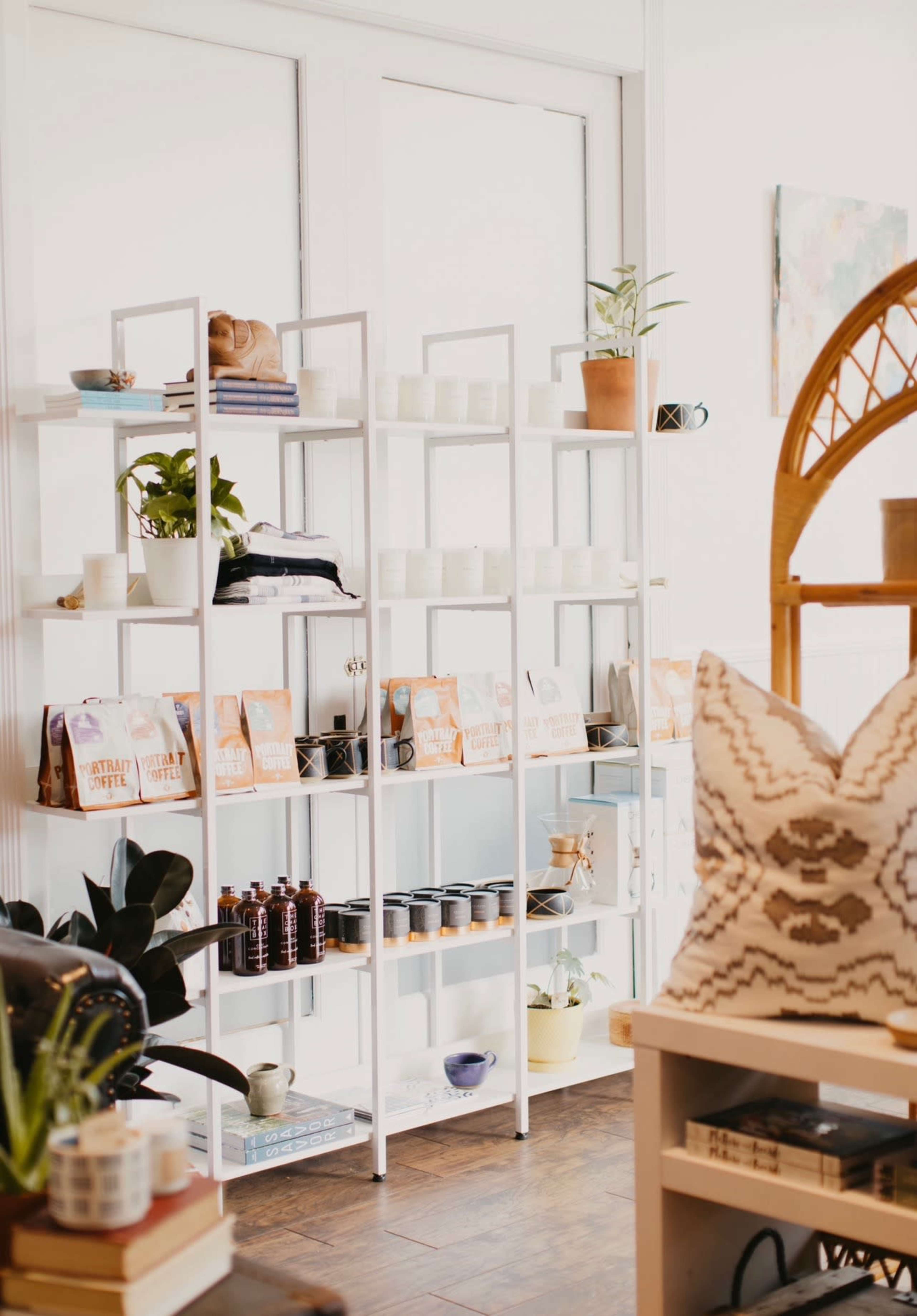 The image shows a neatly organized display of shelves featuring plants, candles, and various packaged items in a brightly lit room.